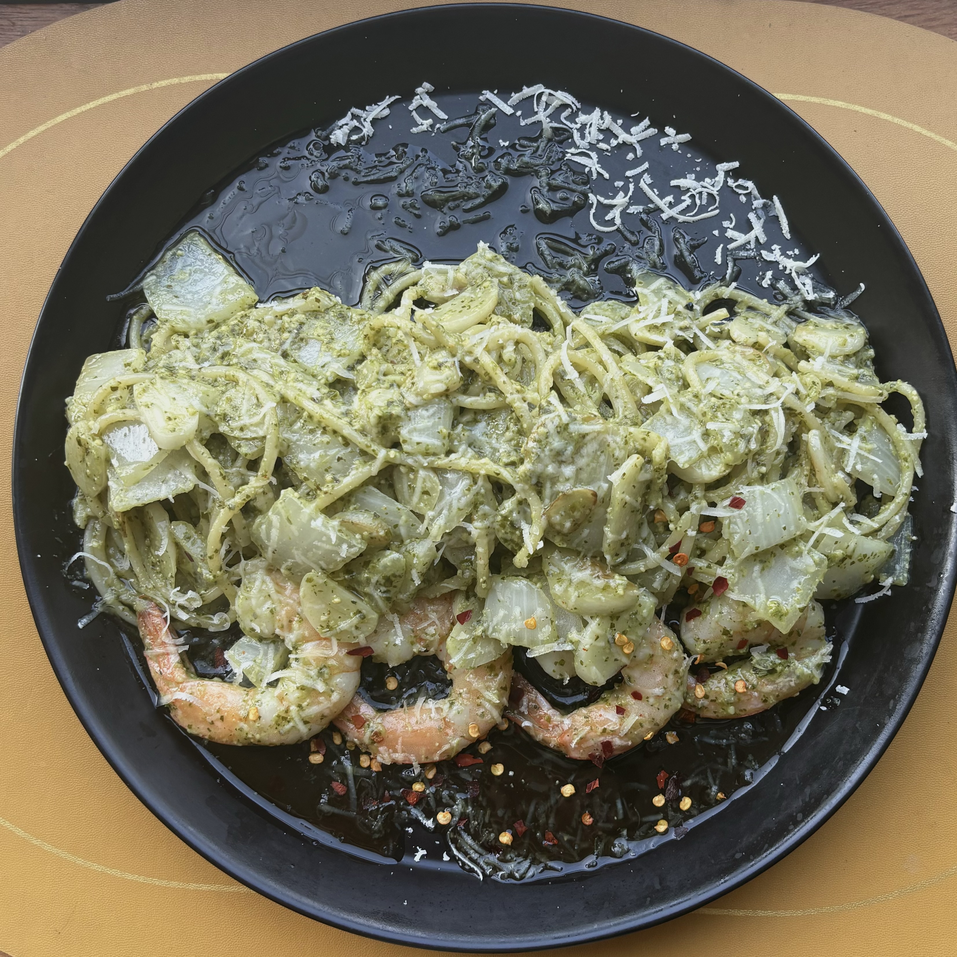 Pesto pasta with shrimp and chili flakes on black dish