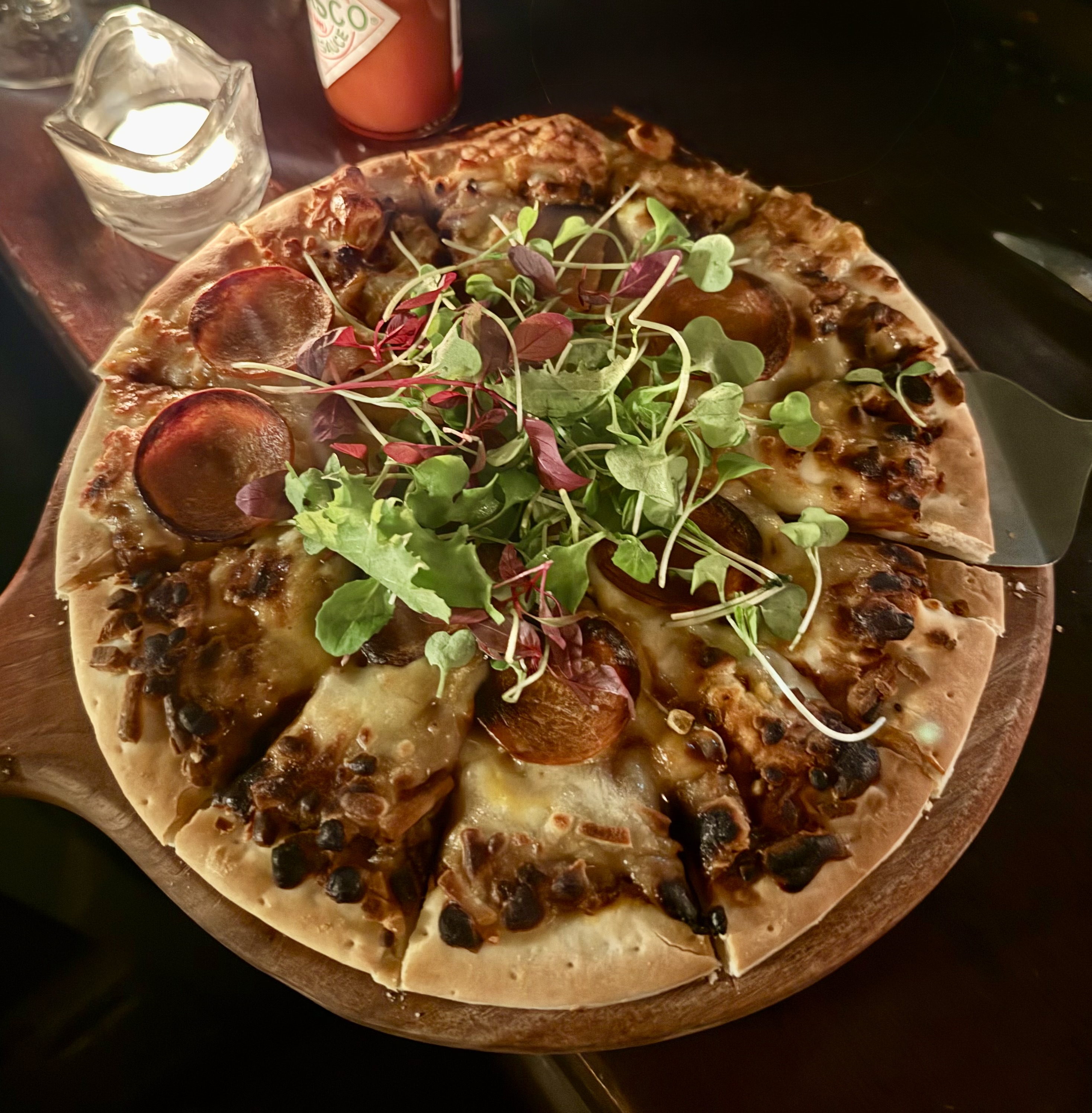 Pepperoni pizza topped with mixed baby greens on a wooden serving board