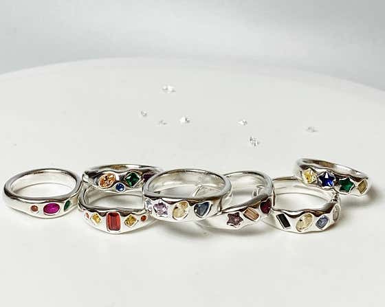 A collection of silver rings set with small colorful gemstones on white surface