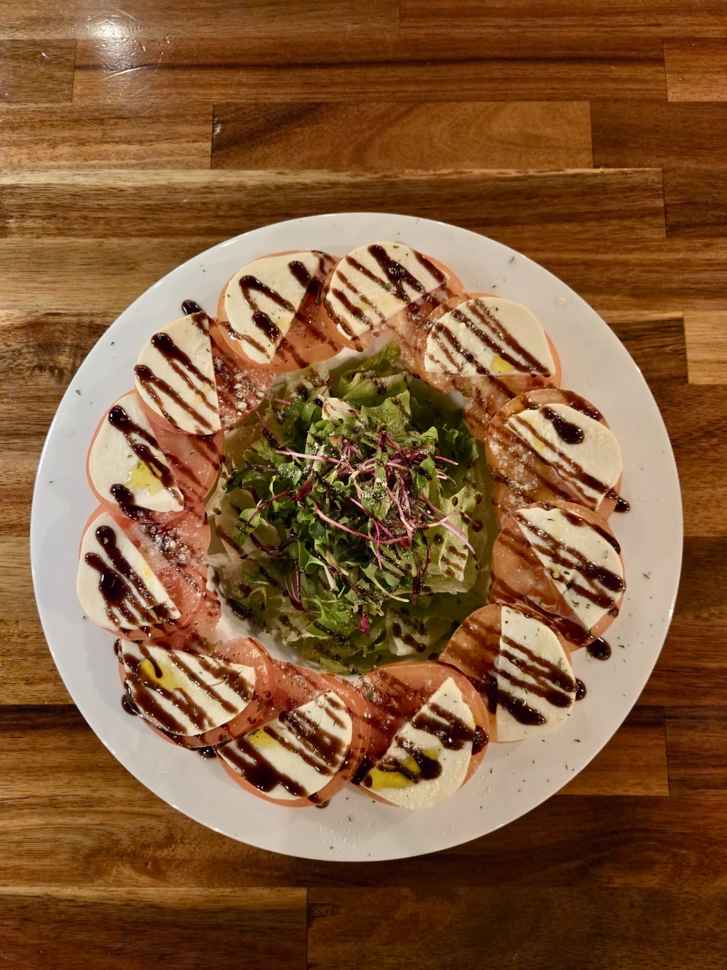 A plate of Caprese salad with tomato, mozzarella, and balsamic glaze on a wooden table