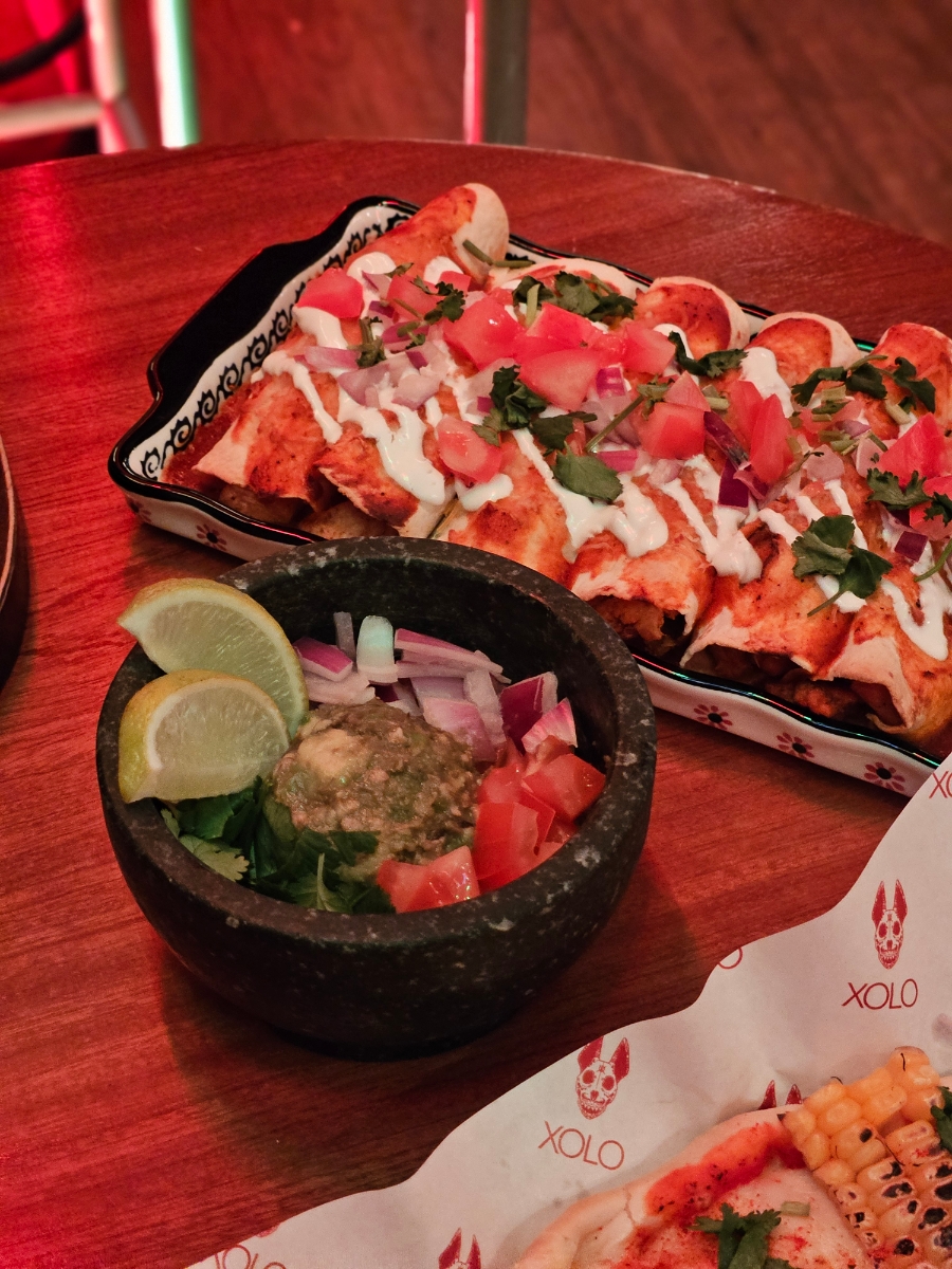 Table spread with molcajete guacamole, enchiladas, and fresh garnishes