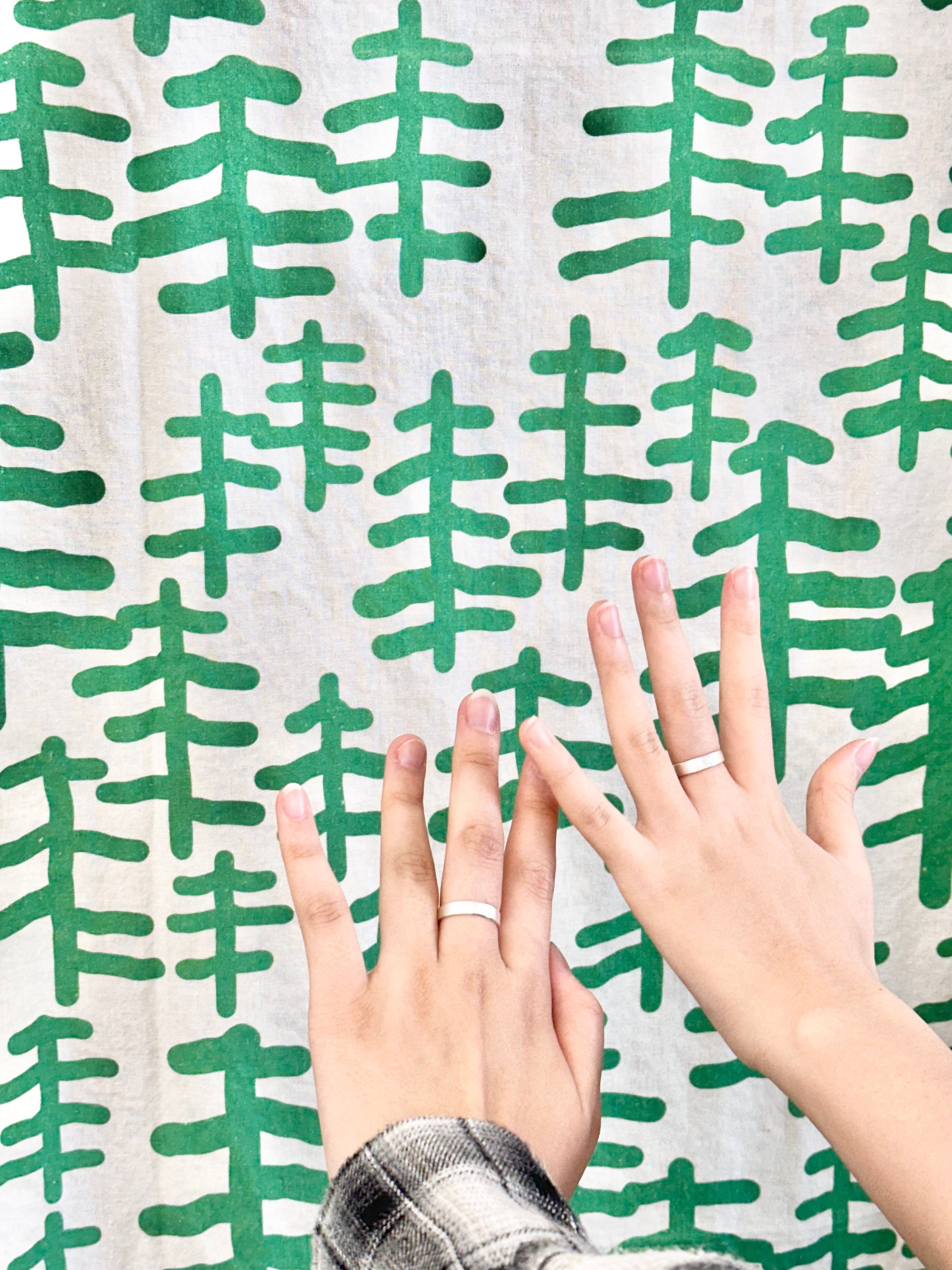 Two hands wearing silver rings against a green tree-patterned fabric background