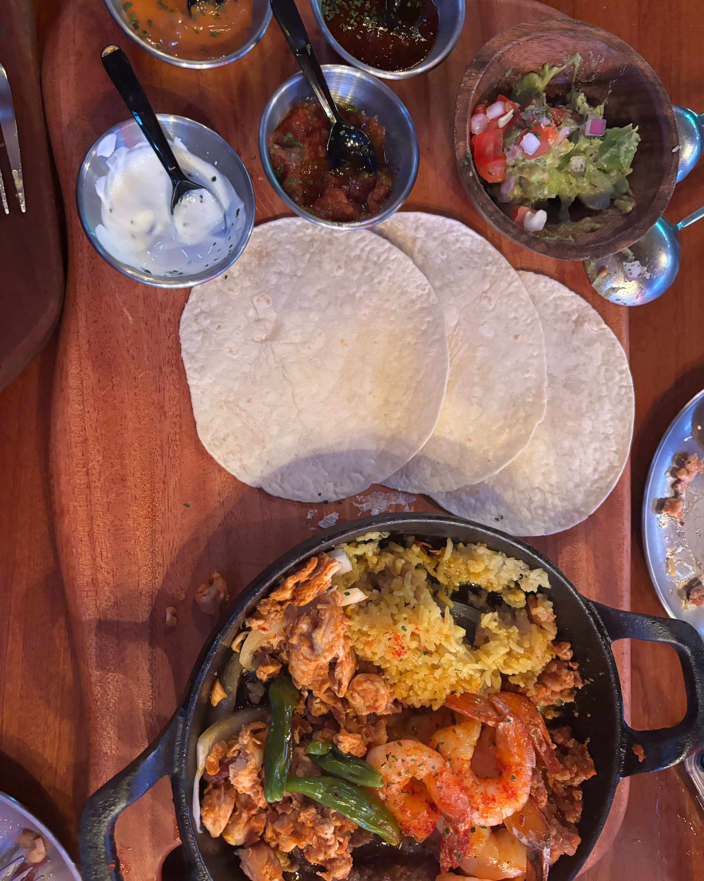 Sizzling fajita iron skillet with seasoned meats, yellow rice, fresh tortillas, and dips
