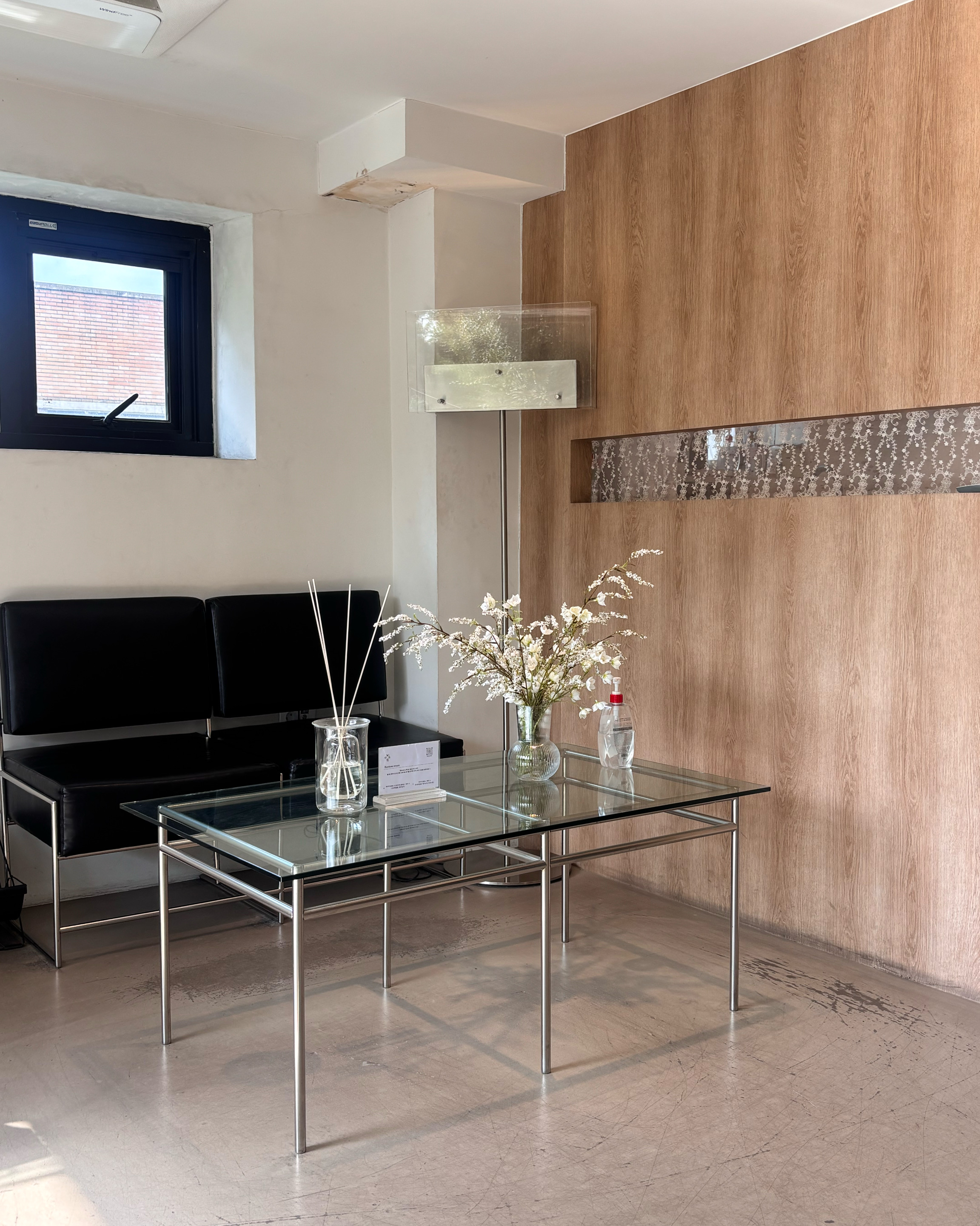 A waiting area with a glass table, sofa, and wooden wall paneling in the studio space