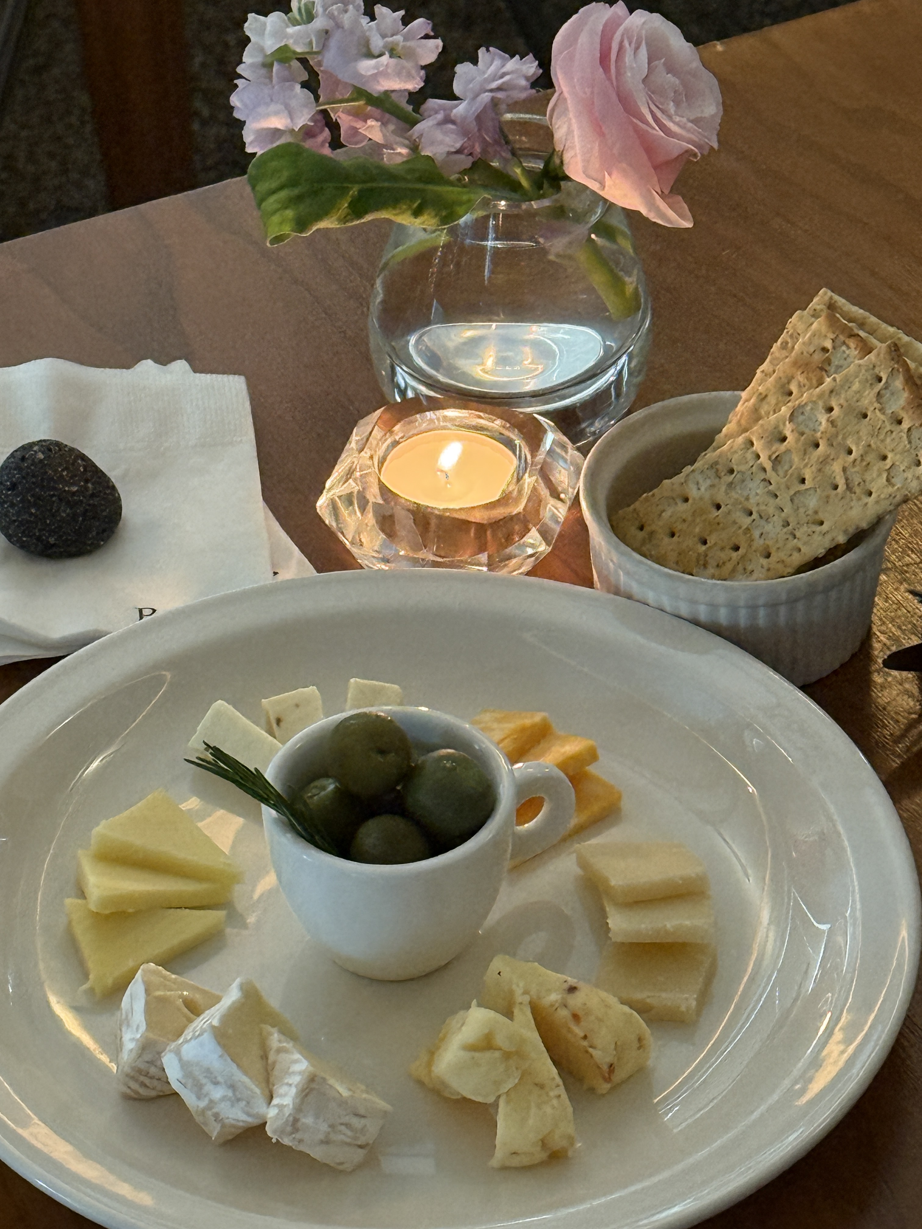 Candlelit wooden dining table with artisanal cheeses, green olives, and fresh flowers
