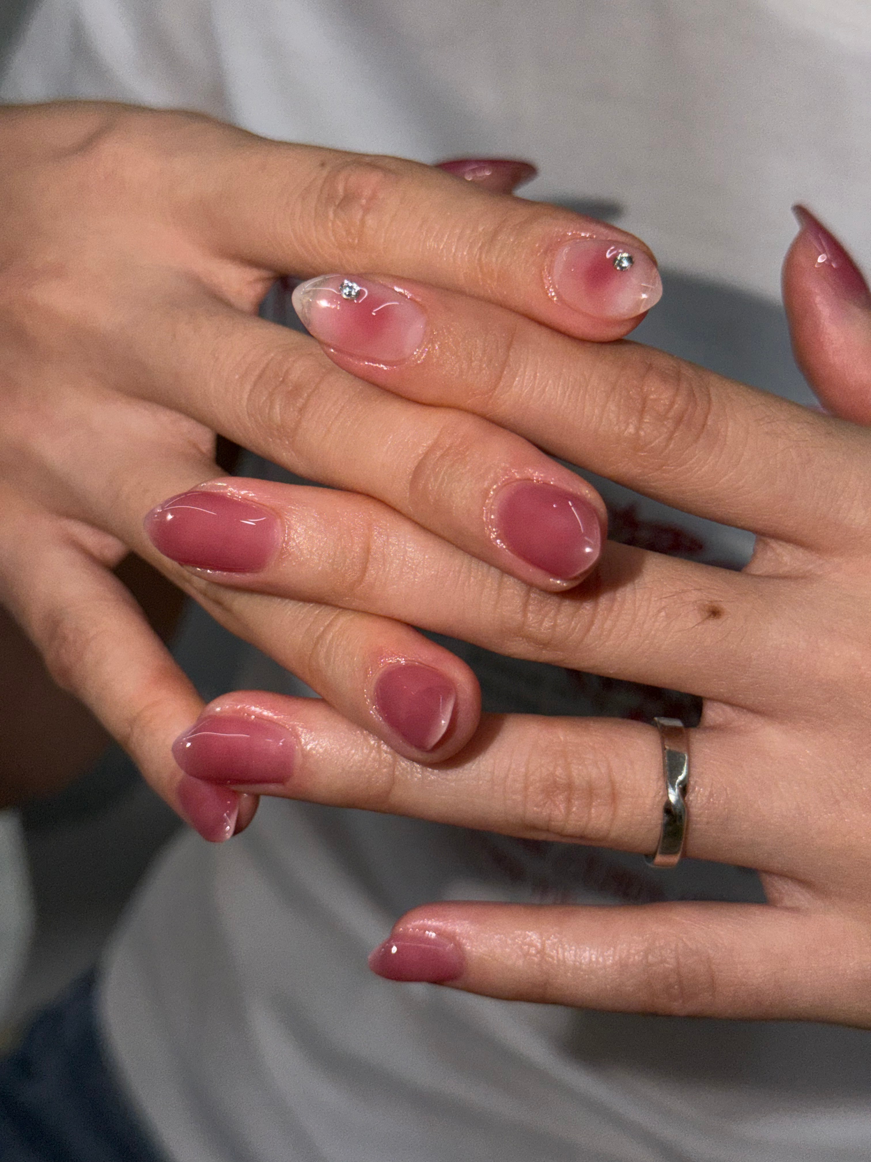 Close-up of hands with glossy pink gradient nail art and small rhinestone accents