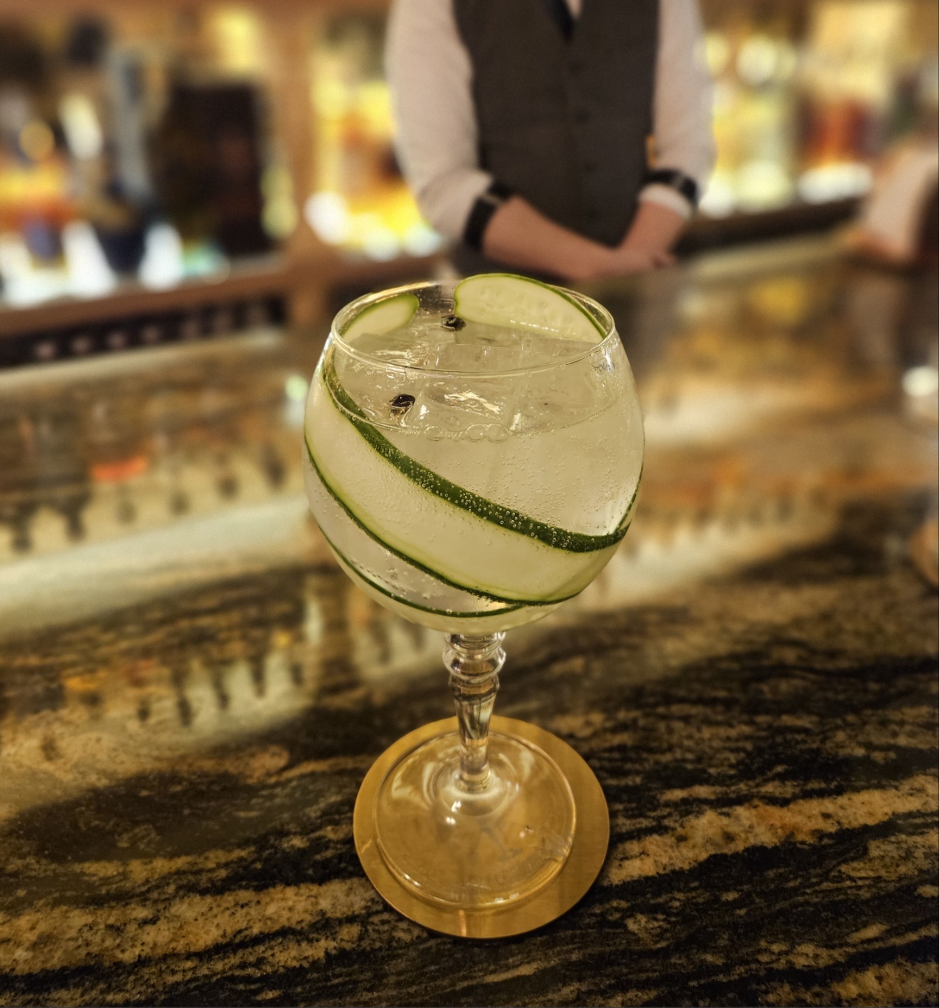 Stemmed cocktail glass with spiraled cucumber ribbons on a marble bar counter