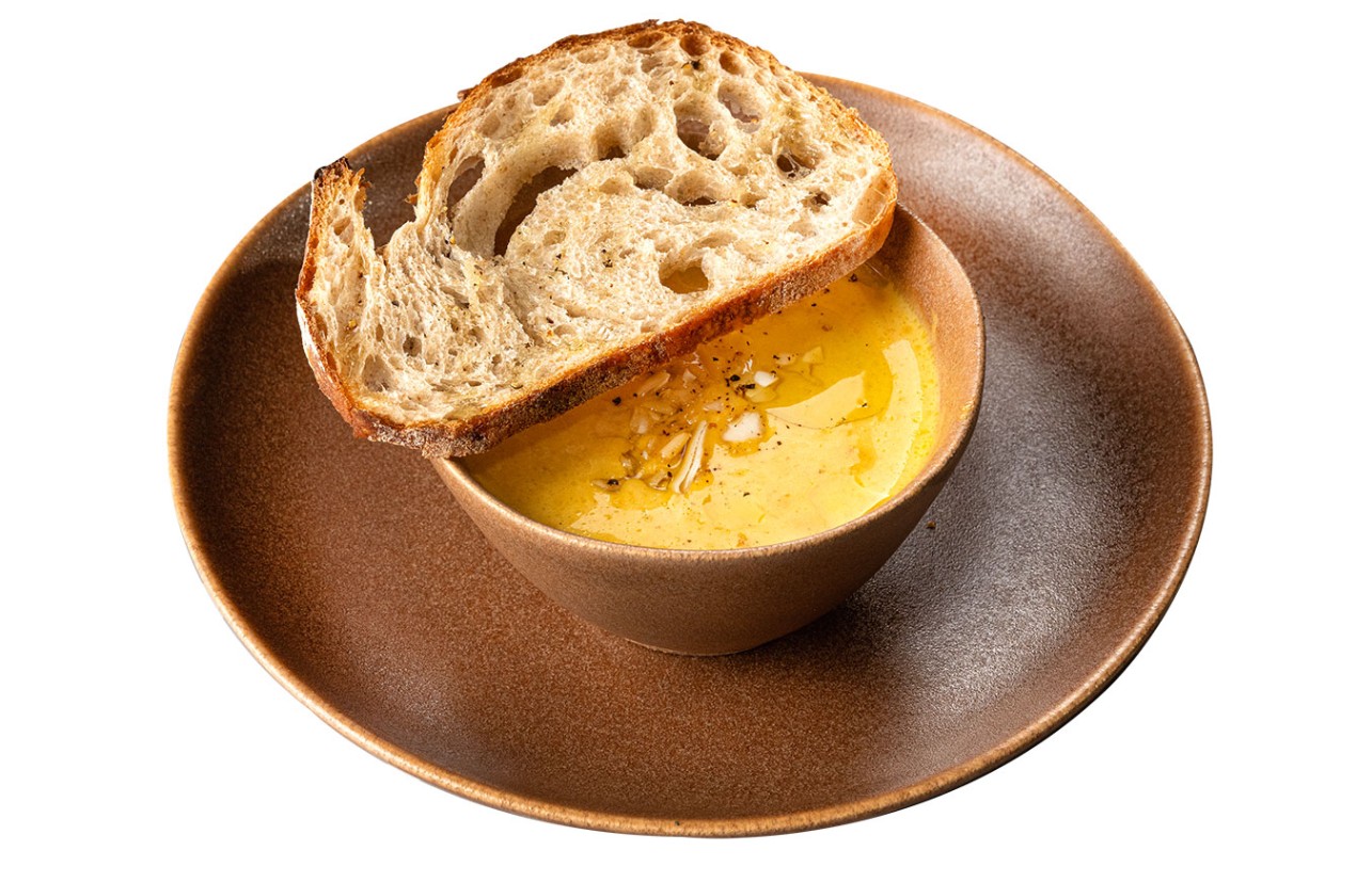 Creamy yellow soup garnished with olive oil and paired with rustic artisan bread
