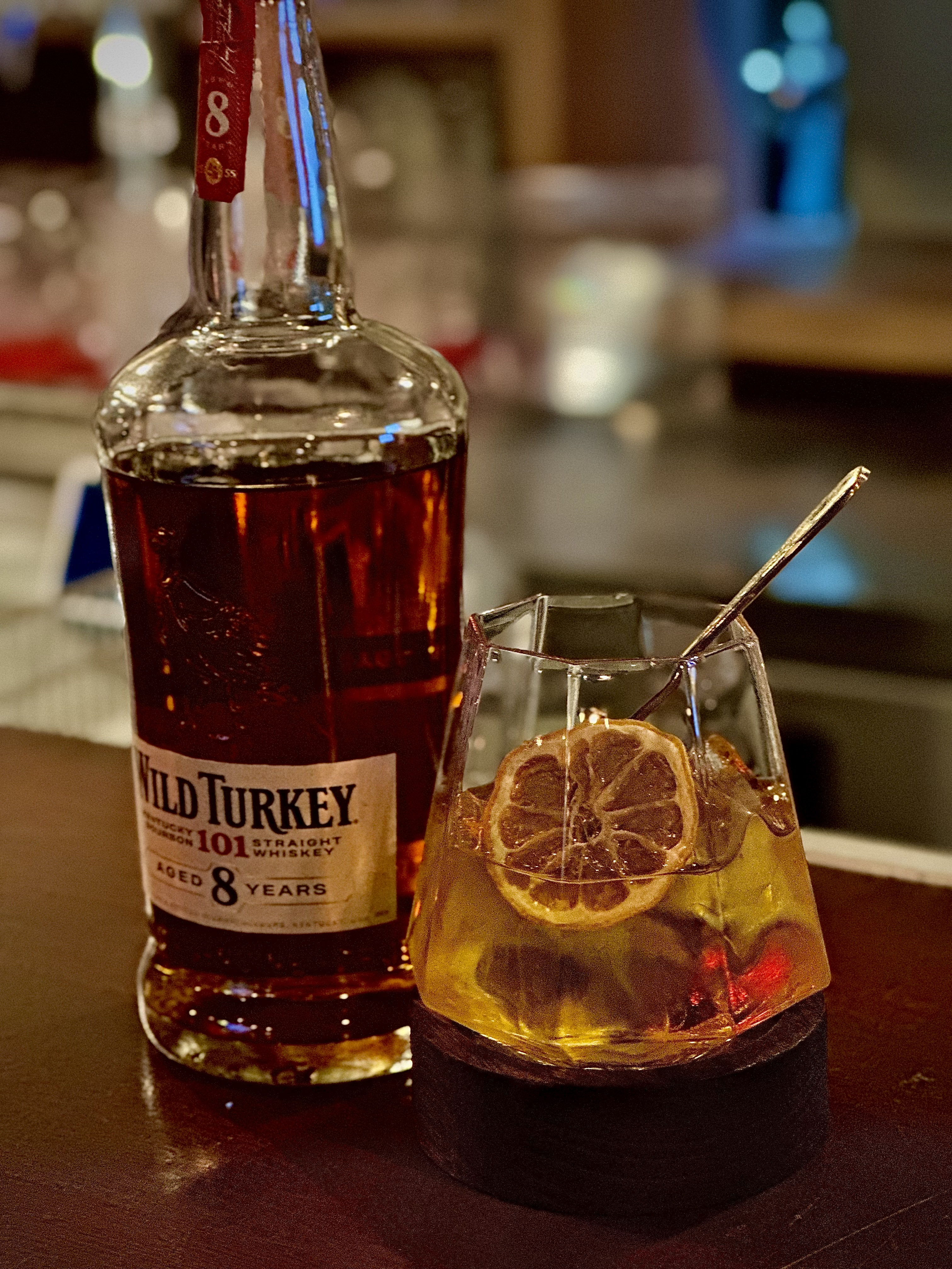 Wild Turkey 101 bourbon next to a whiskey cocktail with a dried lemon slice