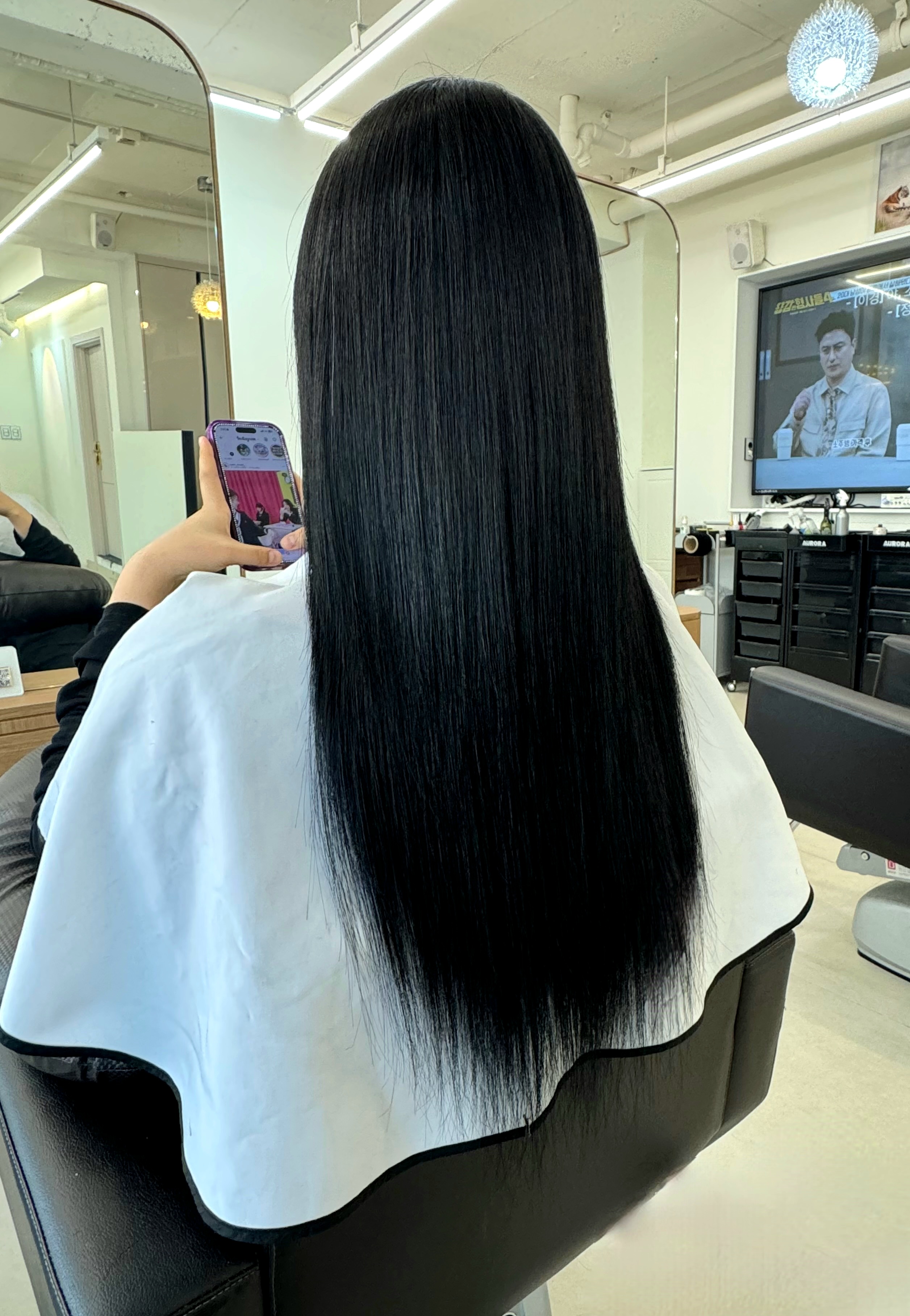 Rear view of a person with long straight jet-black hair extension transformation in salon chair