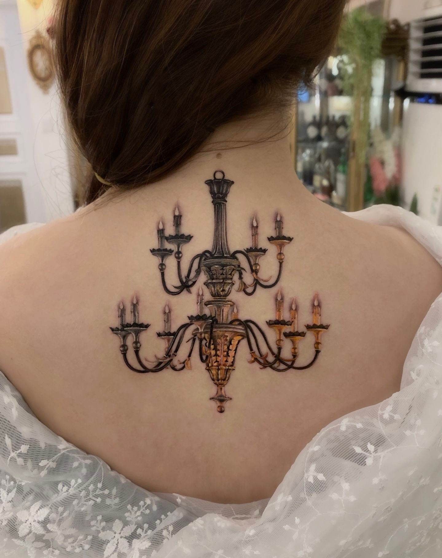A detailed chandelier tattoo on a person's upper back, centered between the shoulders.