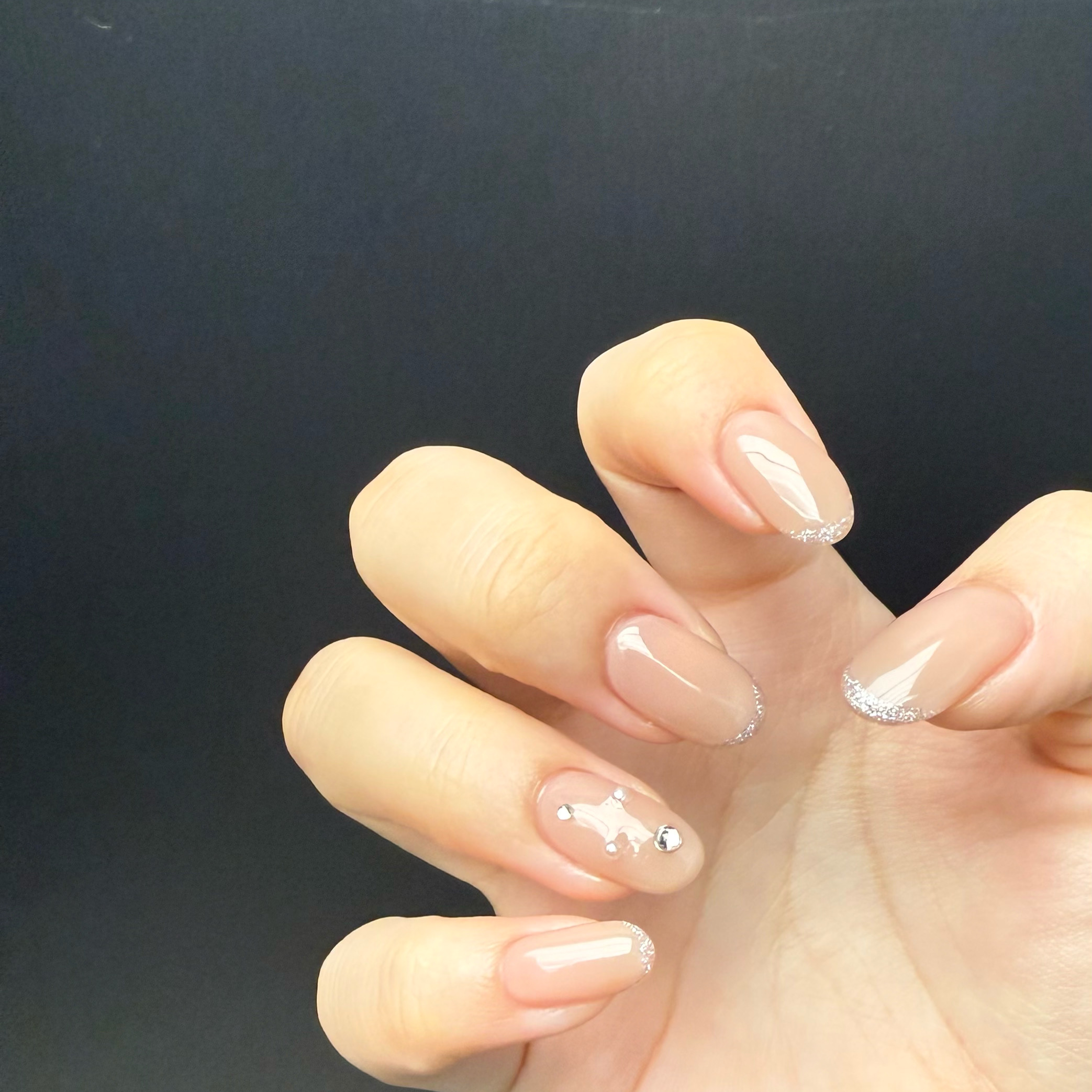 Nude gel manicure with delicate silver glitter tips and rhinestone detailing