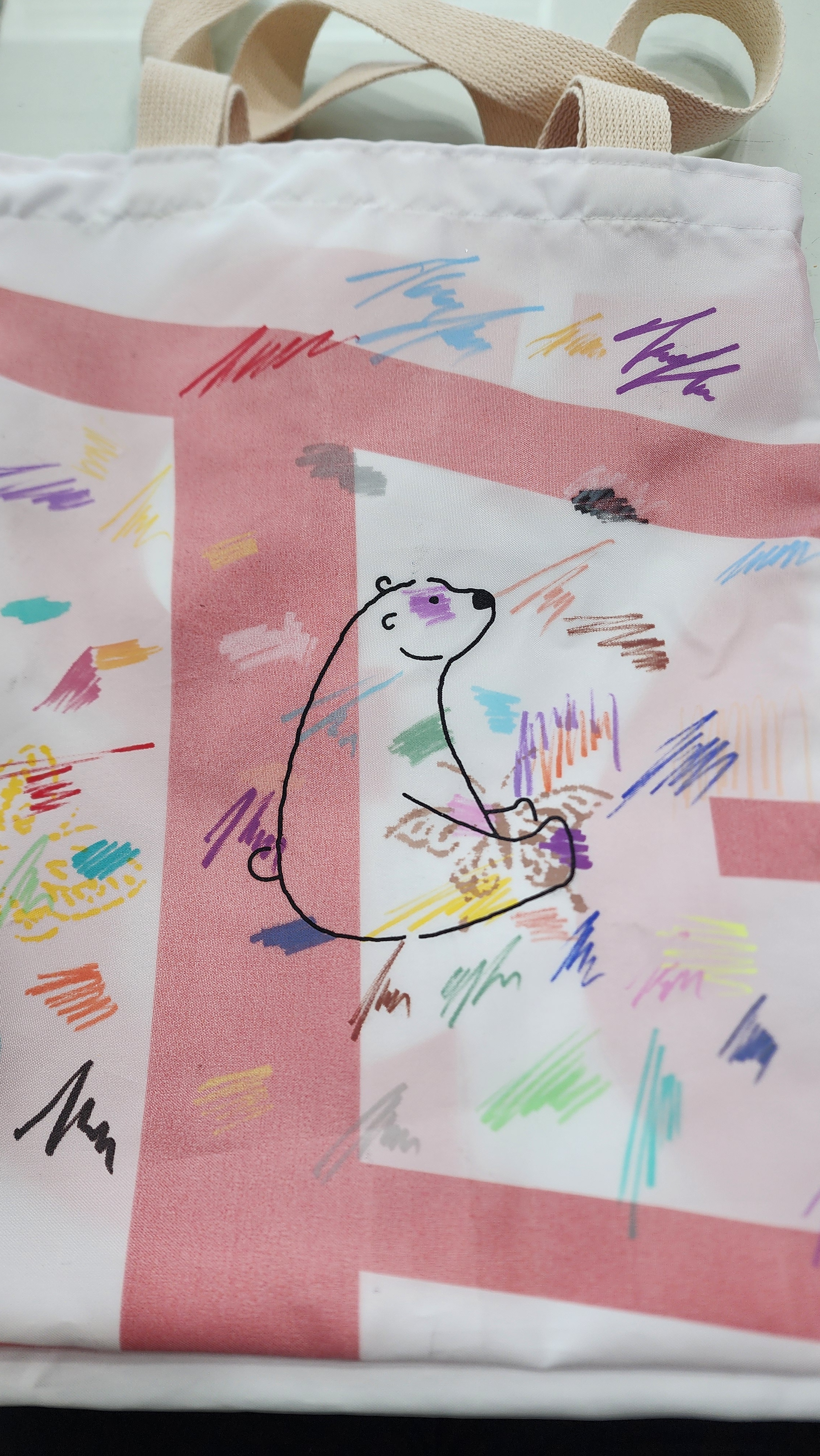 A white tote bag decorated with a simple polar bear illustration and colorful scribbles and patterns.