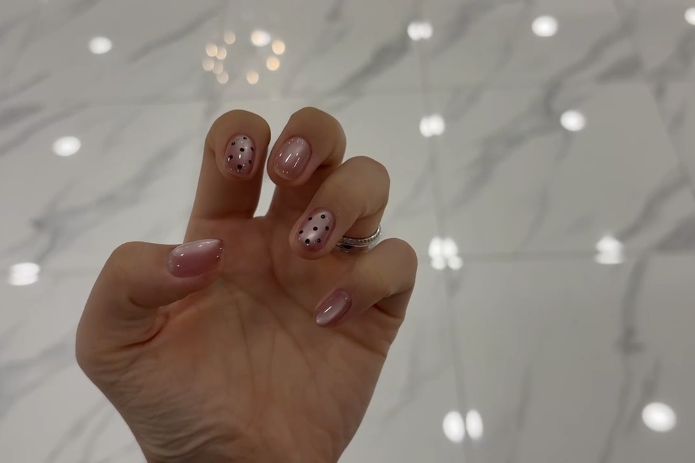 Minimalist iridescent pink nail art with delicate black dot accents
