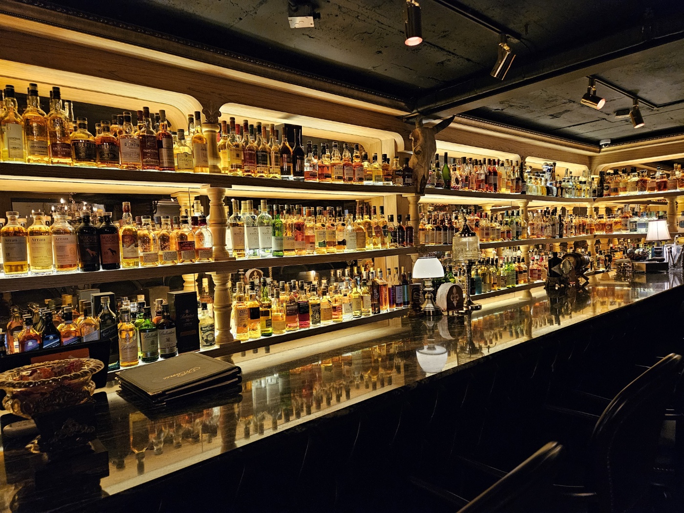 Tiered illuminated bar shelves reflecting across the polished dark countertop