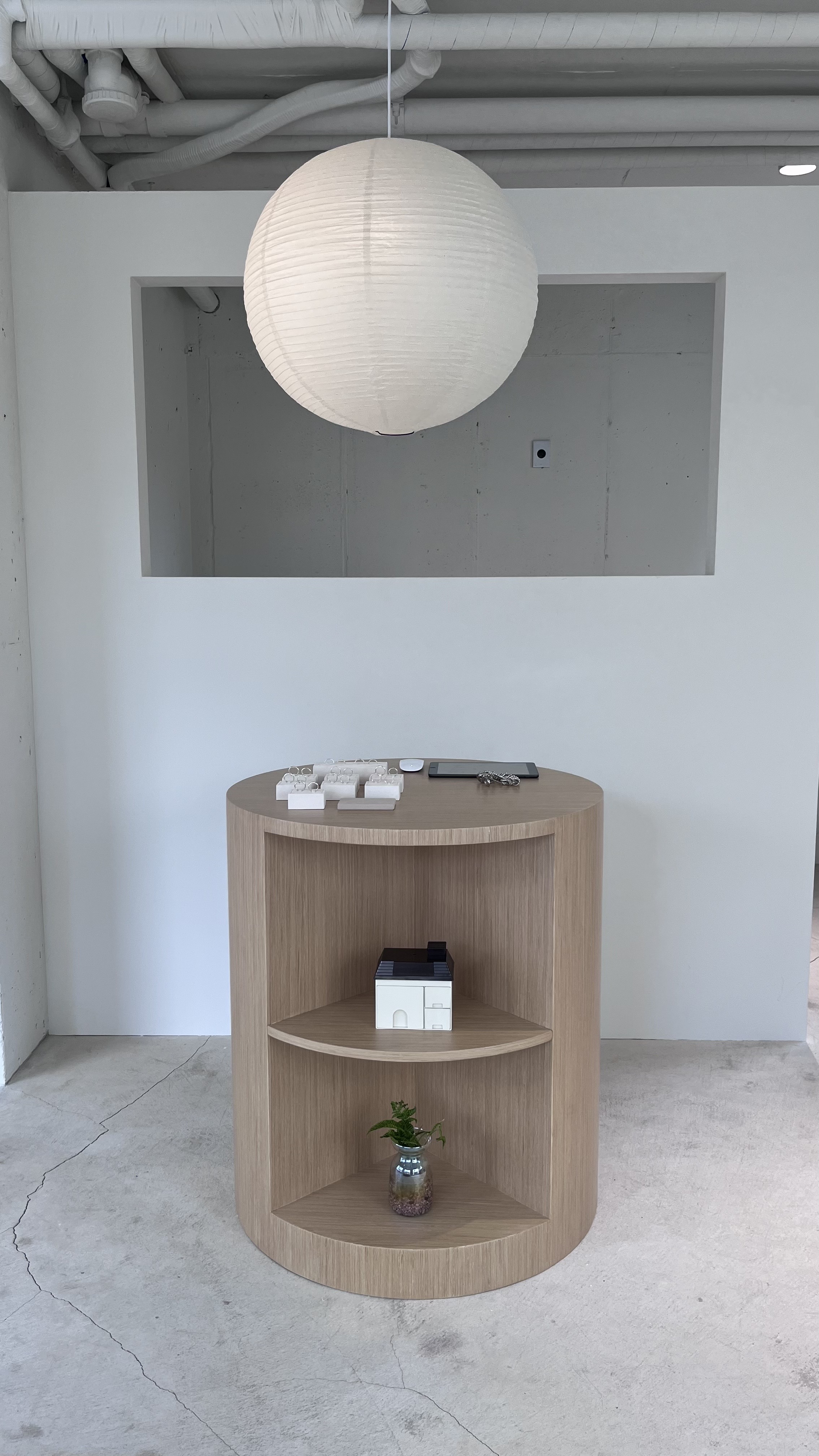Cylindrical wooden display table in front of white wall with round paper sphere lantern.