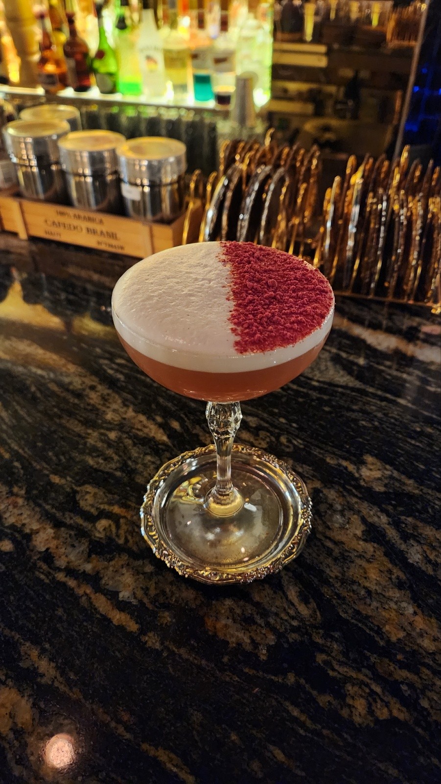 Craft cocktail in a coupe glass with foam and garnish on a silver coaster