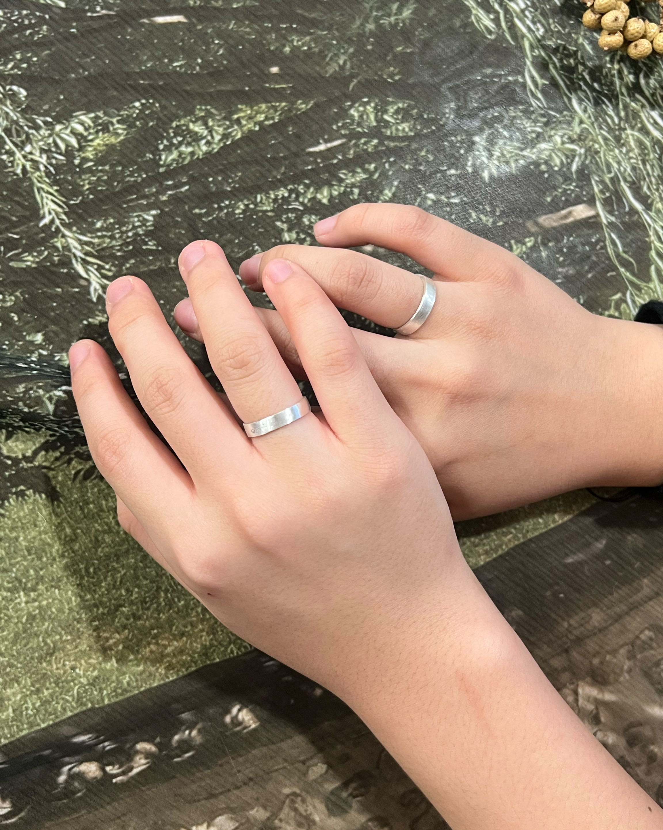 Two hands wearing matching simple silver rings resting on a table surface