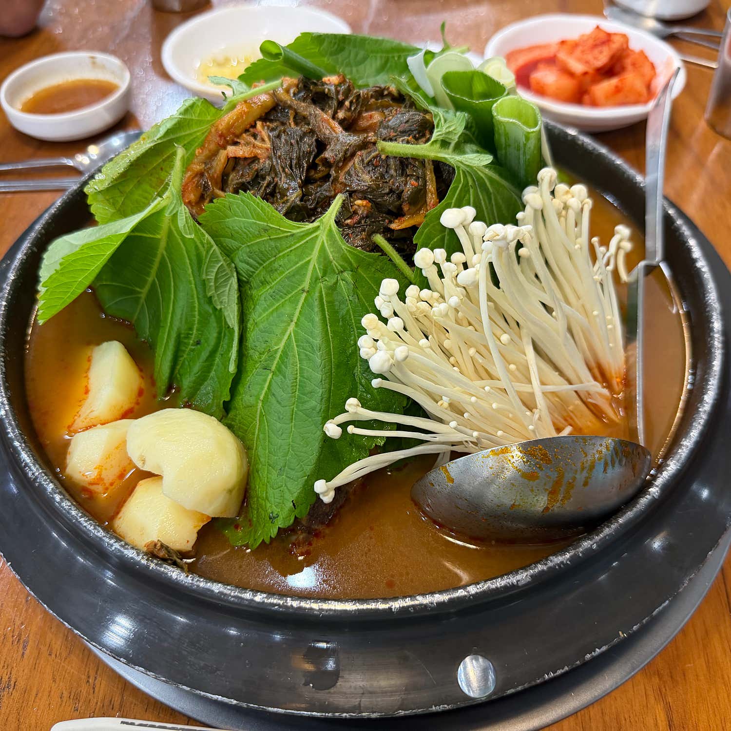 A close-up of a bubbling pot of Gamjatang, a traditional Korean pork bone soup with leafy greens, mushrooms, and potatoes.
