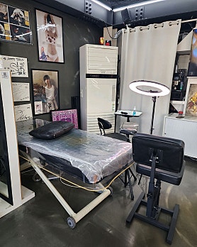 Medical-grade tattoo procedure room with clinical bed, ring light, and sanitized trolley
