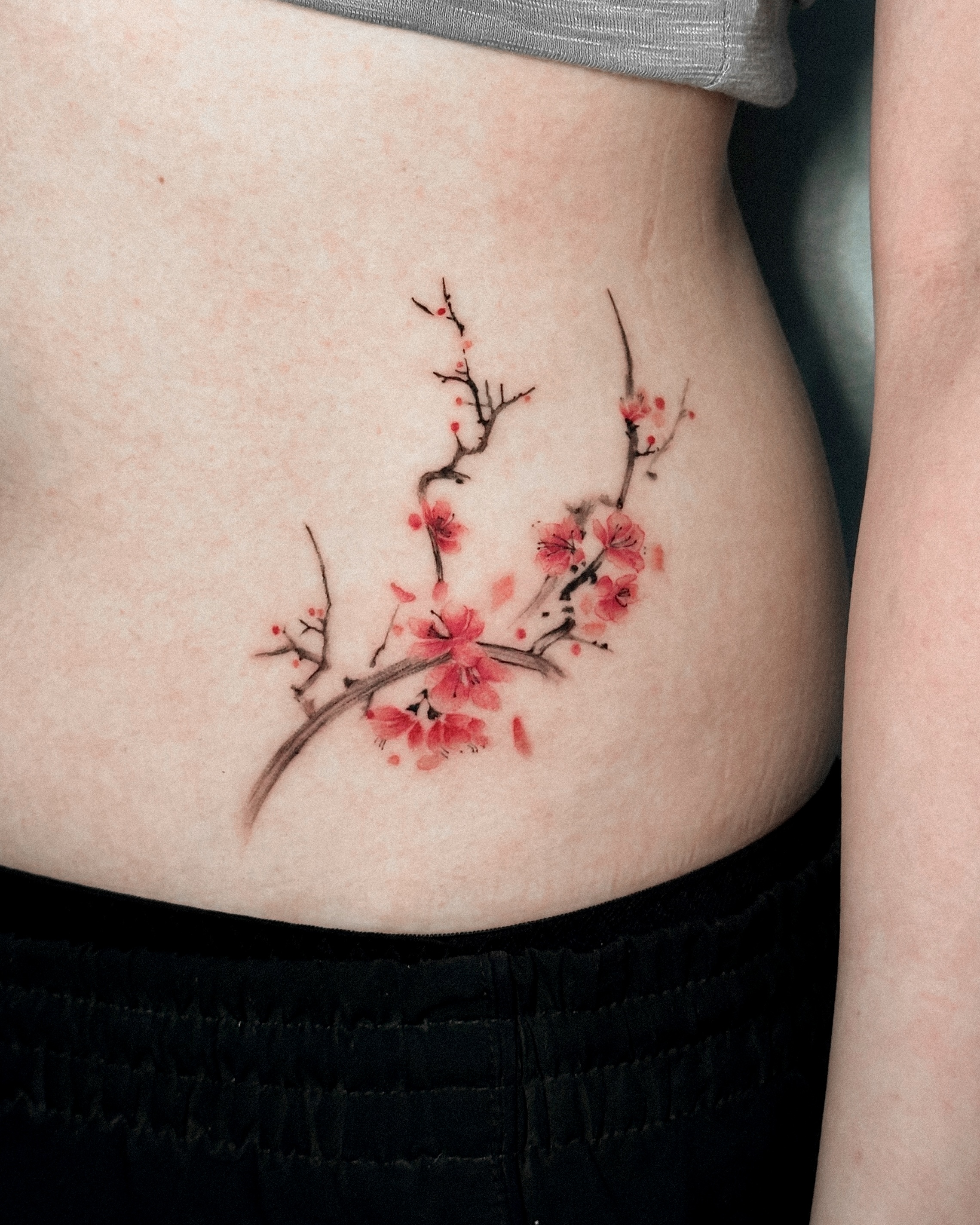 Delicate watercolor-style cherry blossom tattoo on torso in Asian brush style
