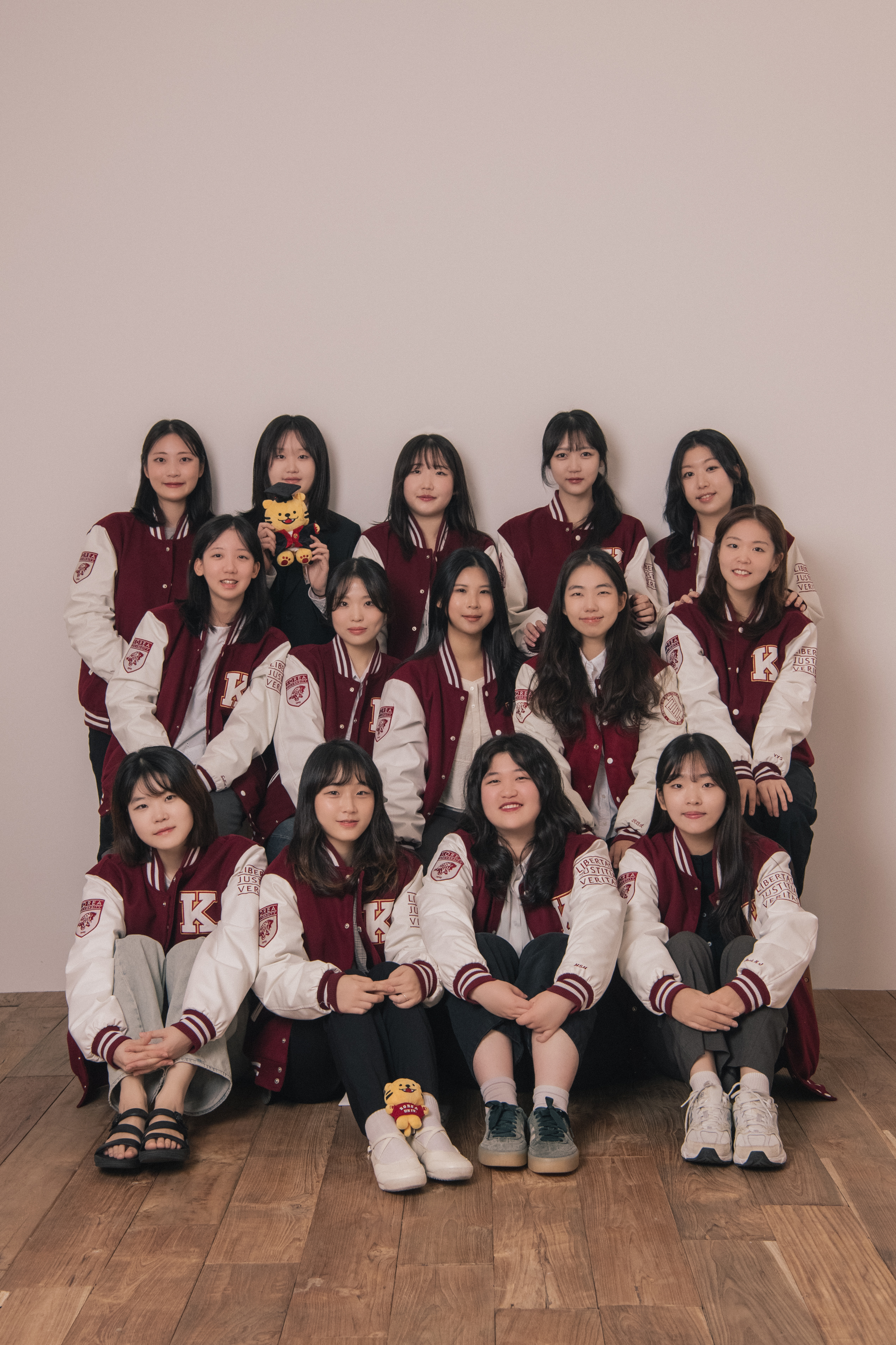 A group of young women wearing maroon and white university varsity jackets posing for a studio photo