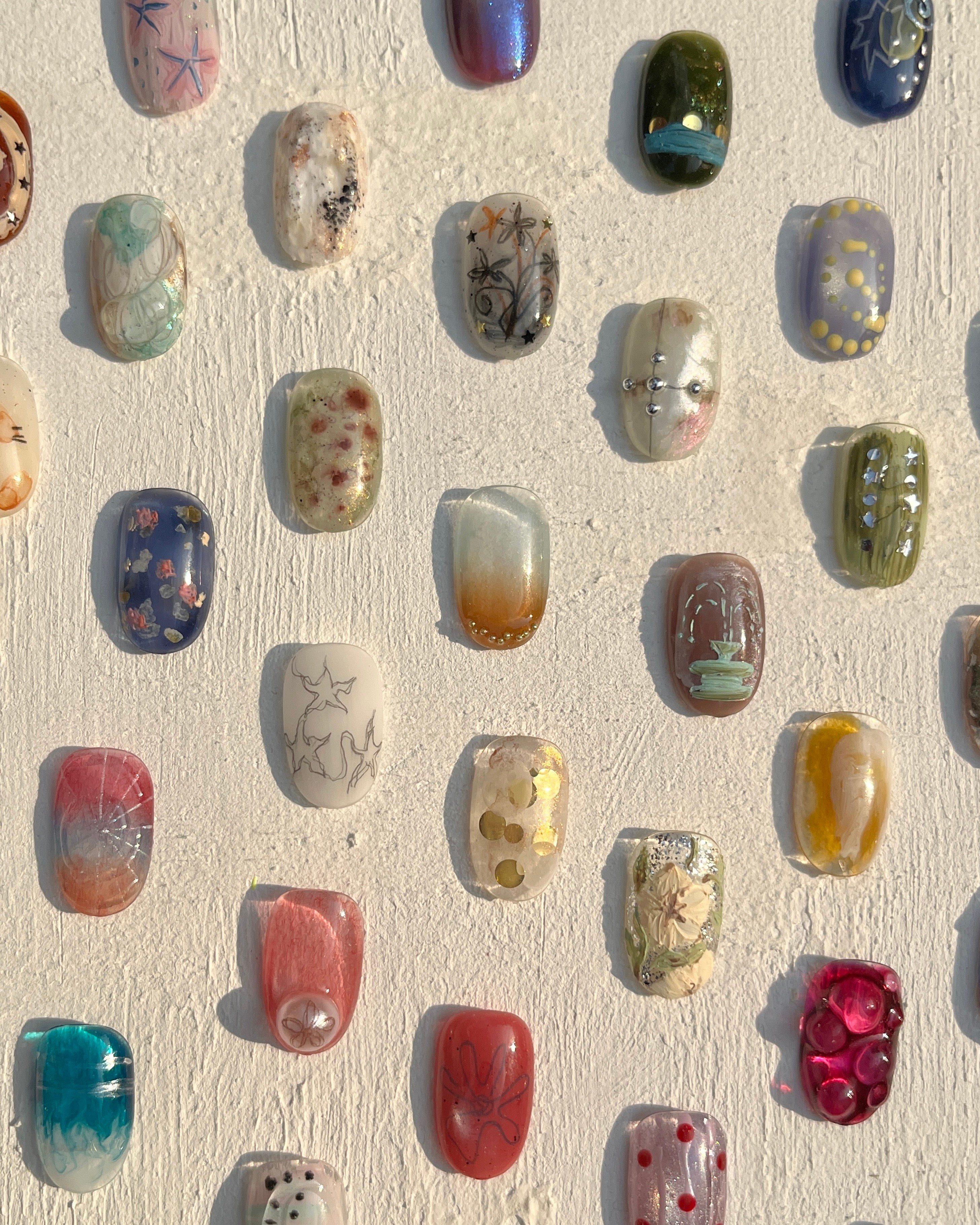 Display of various colorful nail art design samples on textured white background