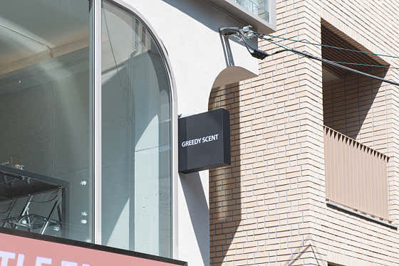 A black square sign labeled GREEDY SCENT mounted on a brick building corner in Yeonnam-dong