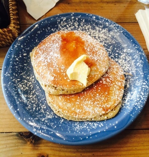 Two golden pancakes with butter and powdered sugar on a blue plate