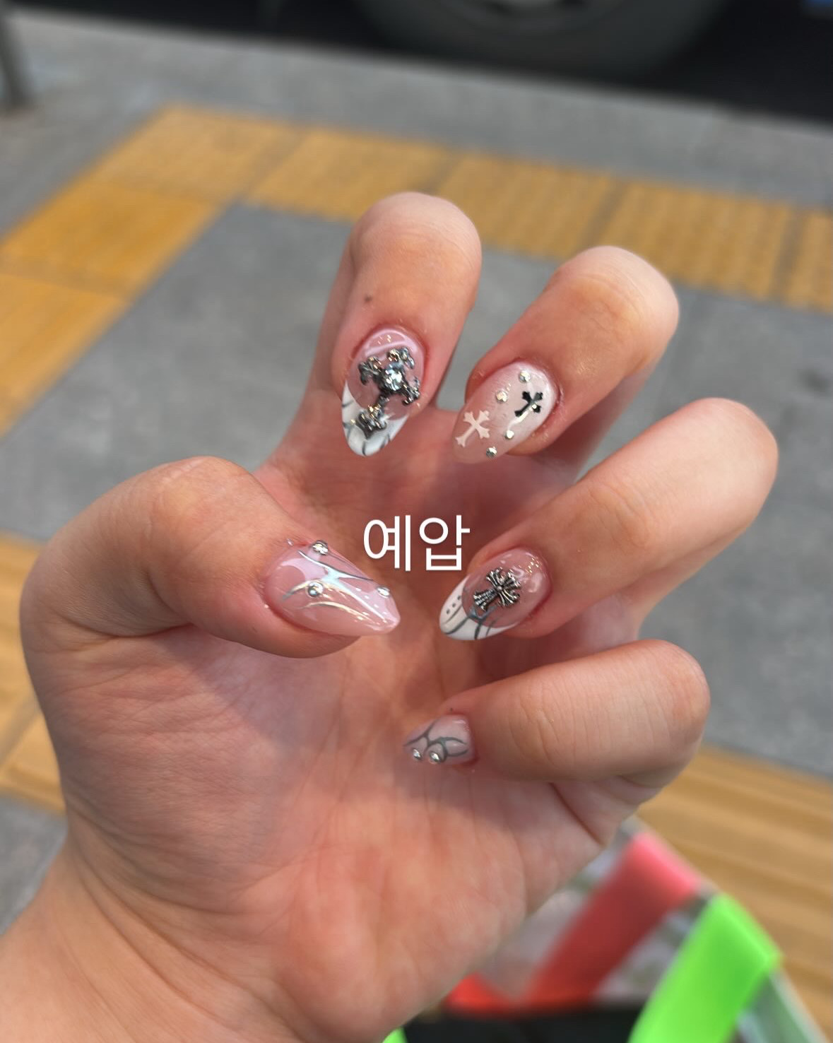 Close-up of a hand featuring detailed nail art with cross-shaped charms and metallic accents