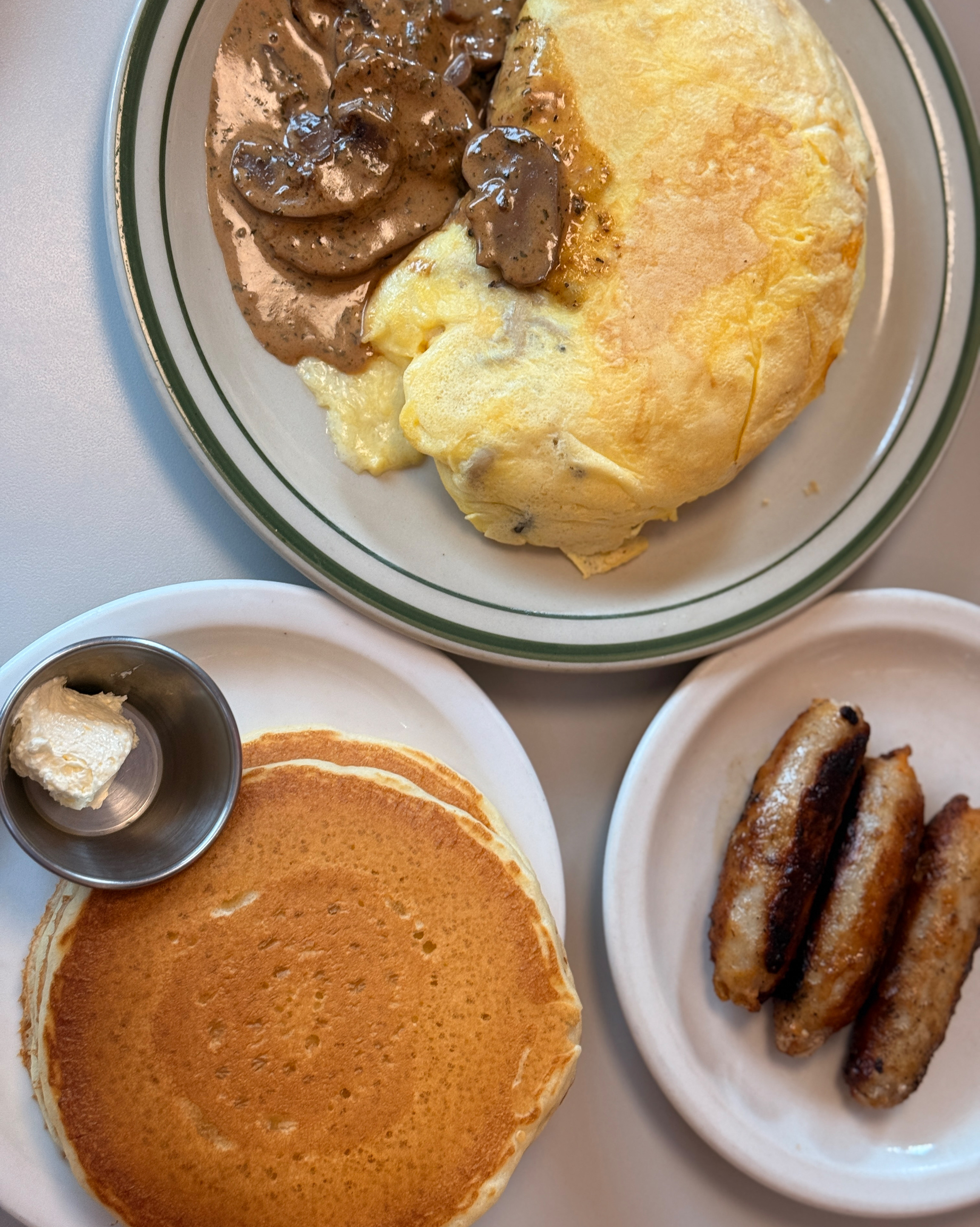 Three brunch plates featuring mushroom omelette, pancake stack with butter, and browned sausages