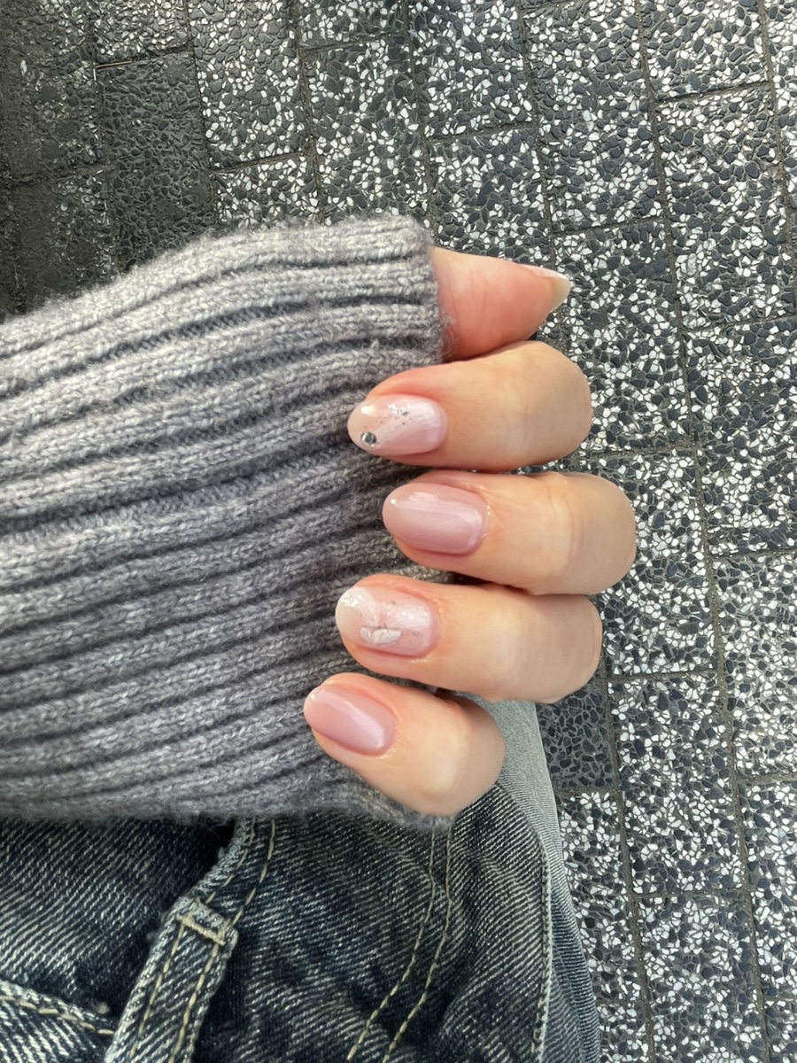 Close-up of hand with manicured nails featuring light pink polish and subtle glitter rhinestone accents