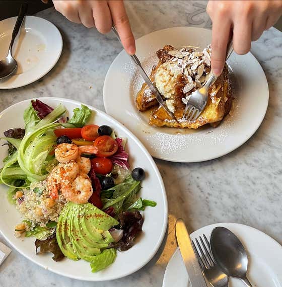 Close-up of hands cutting French toast with shrimp salad on a marble table at Oasis Hannam