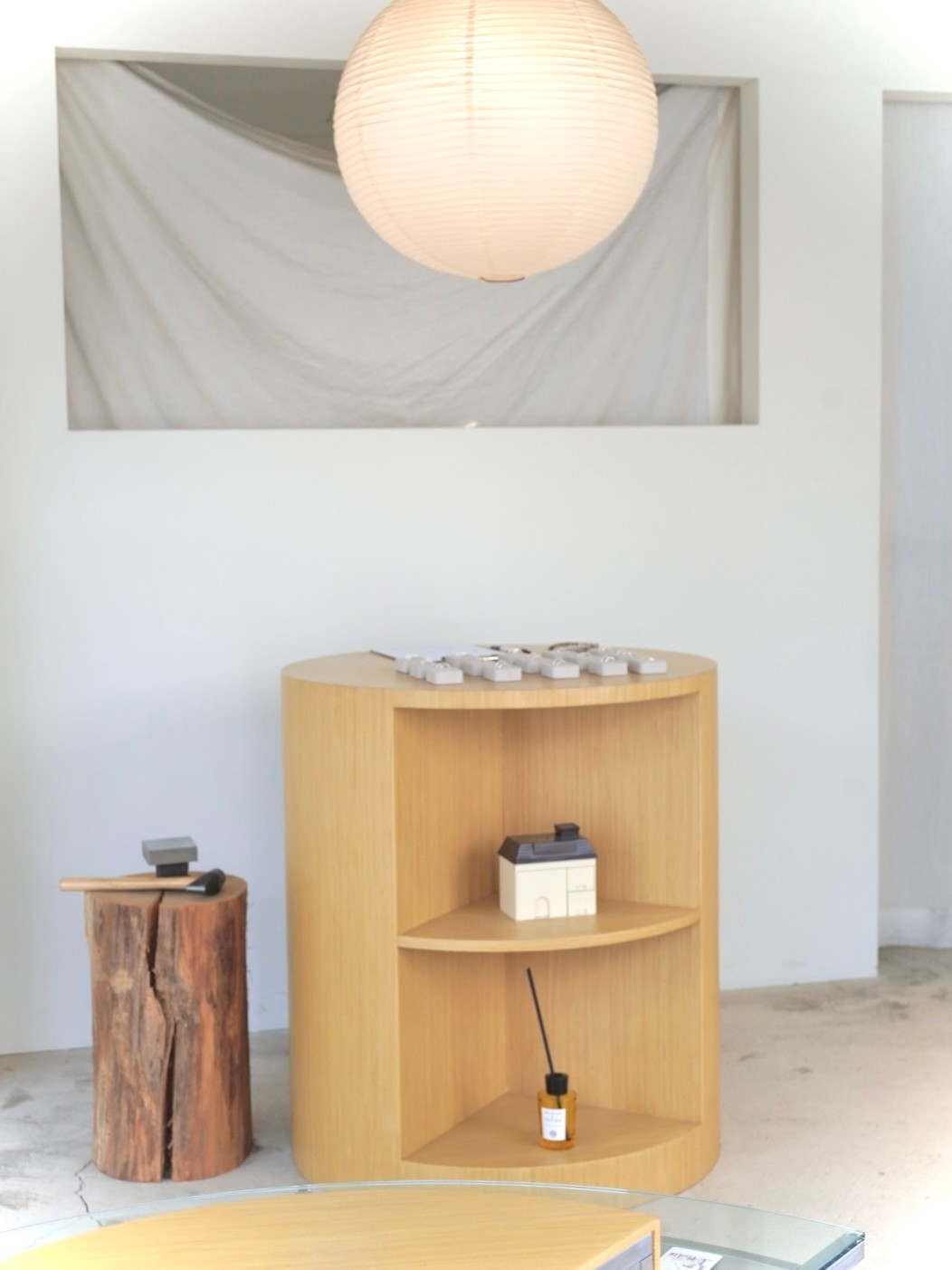 Minimalist workshop interior with a curved wooden display shelf, paper lantern, and timber stump table.