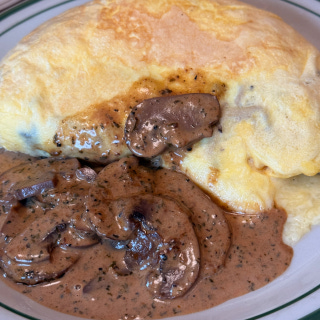 Omelette topped with sliced mushrooms in rich creamy brown gravy