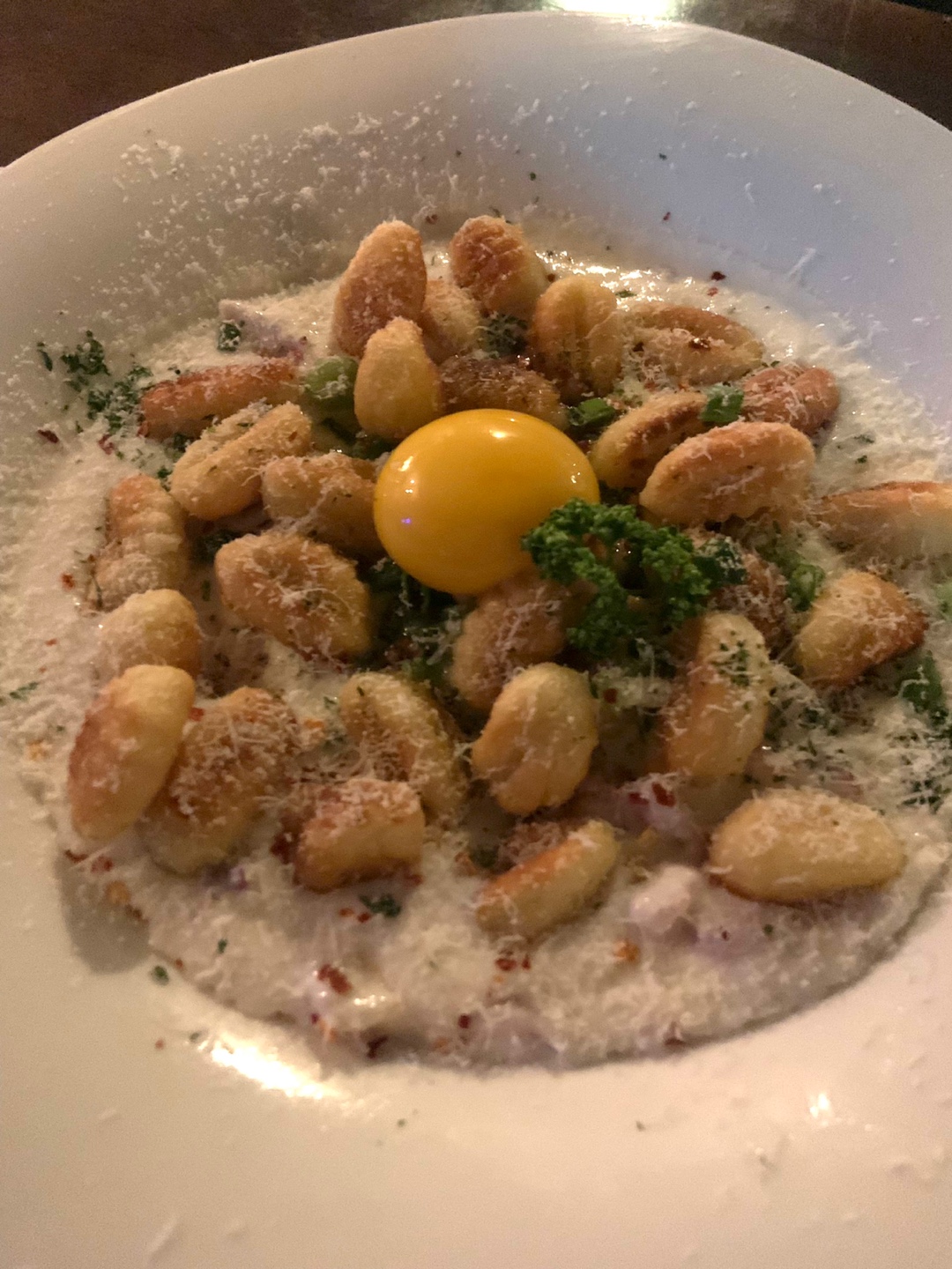 Golden pan-seared gnocchi with creamy sauce, grated cheese, and fresh egg yolk center