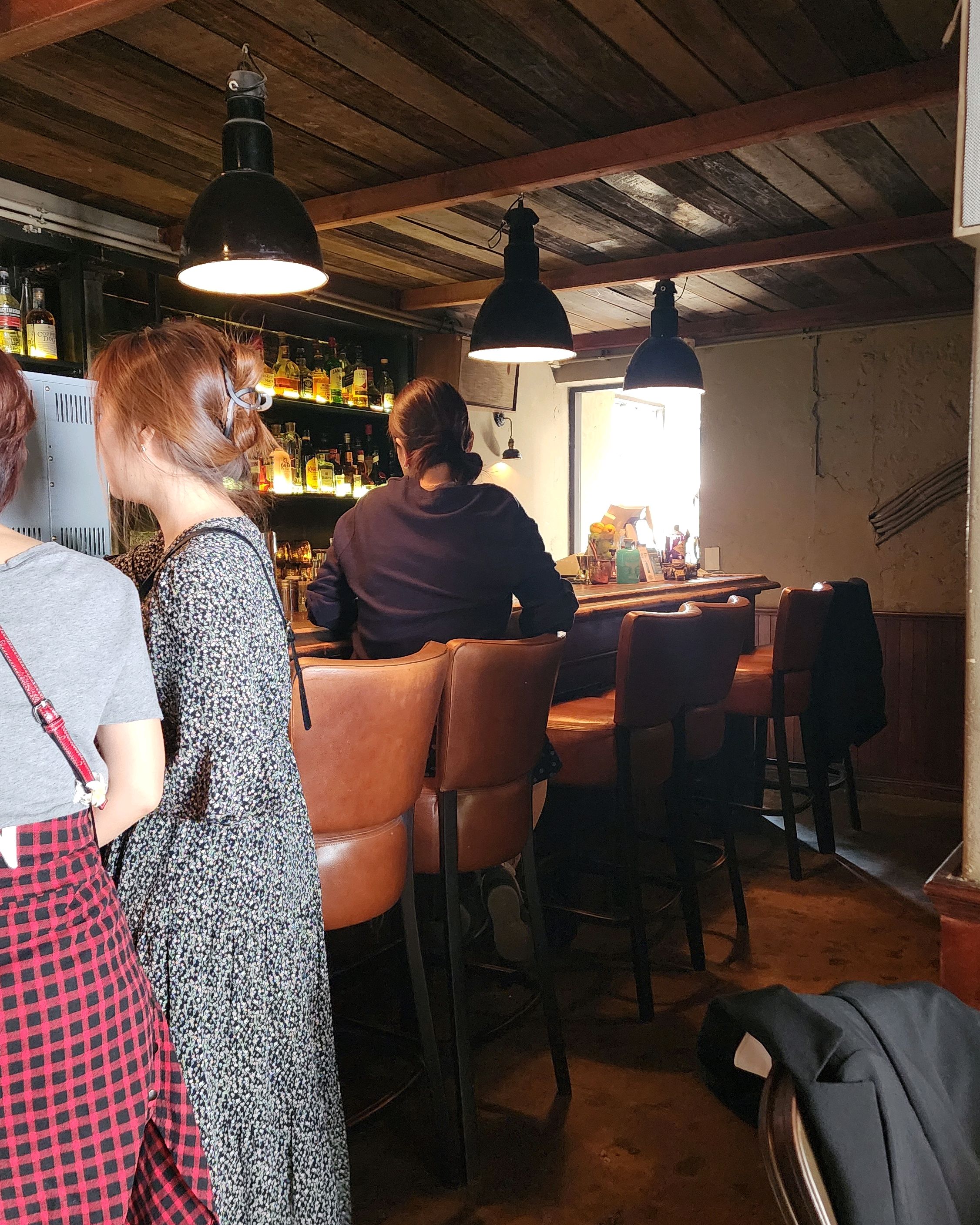 First floor street-connected bar counter with rustic stools and industrial pendant lights.