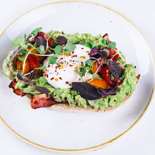 Avocado sourdough toast topped with a poached egg and cherry tomatoes