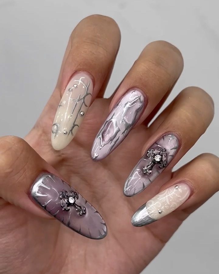 Close-up of long almond-shaped fingernails with metallic, cross-shaped charms and silver swirl nail art designs