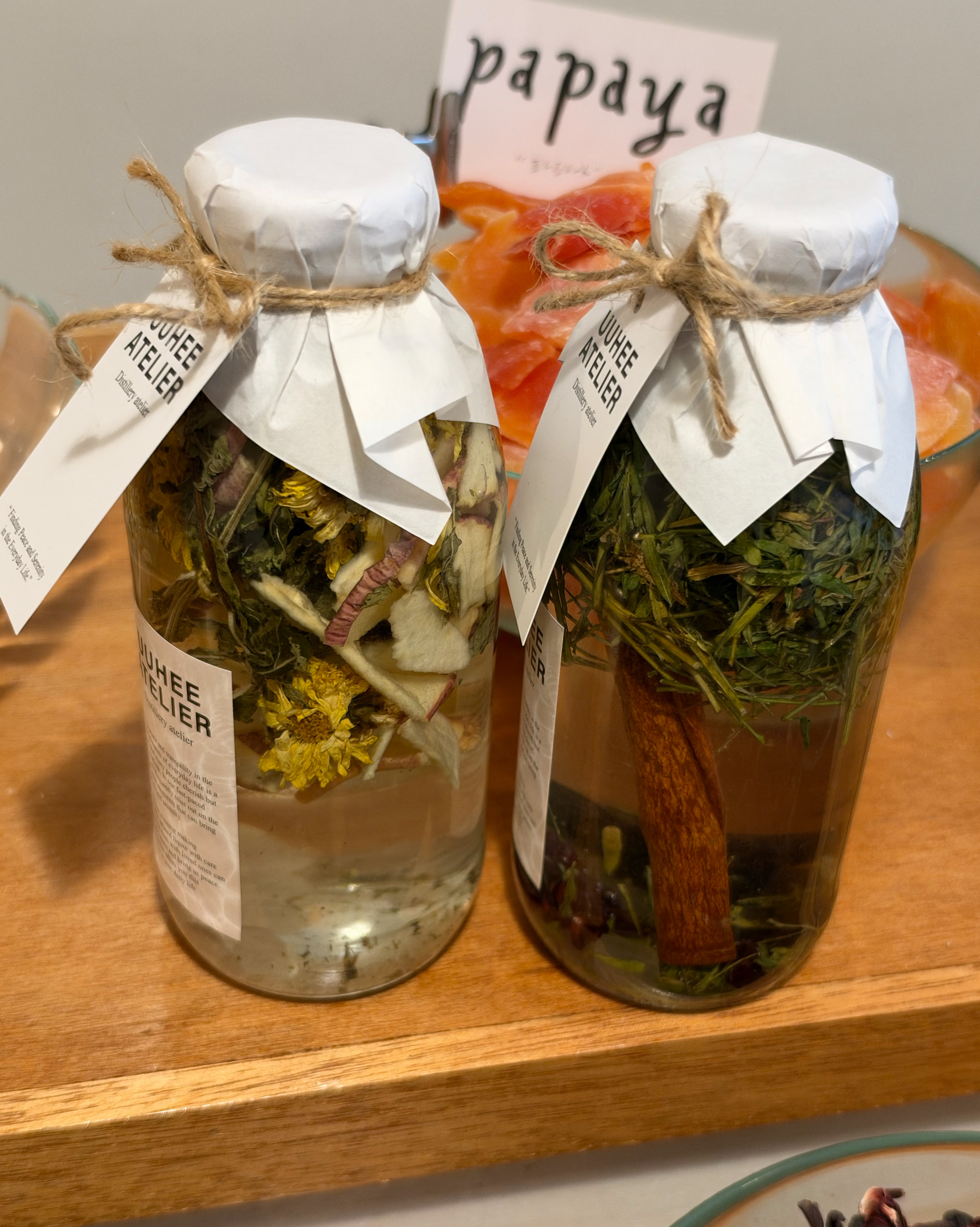 Two glass bottles filled with dried fruits and herbs for infused liquor, displayed on a wooden surface.