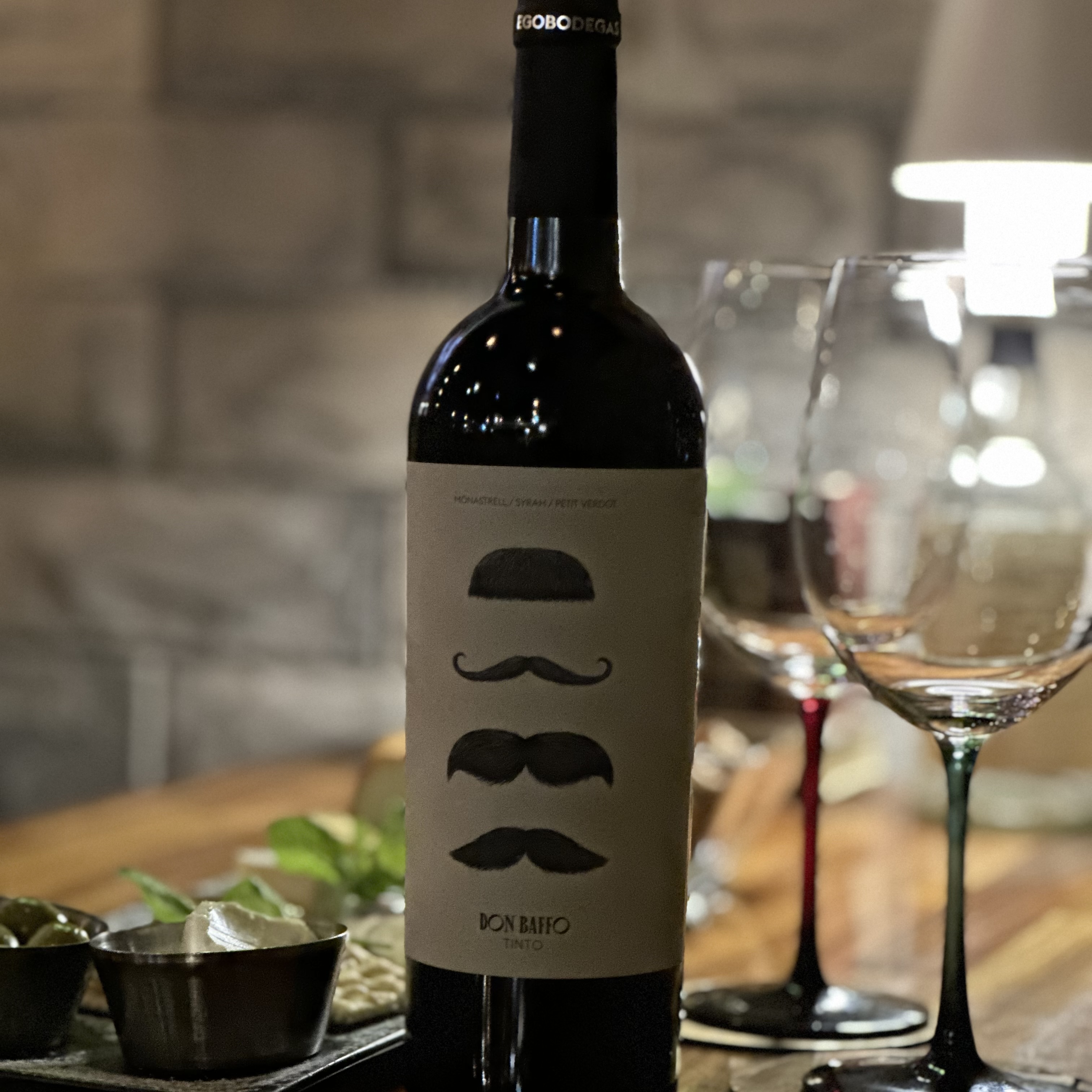 A bottle of Don Baffo red wine sitting on a wooden table with wine glasses