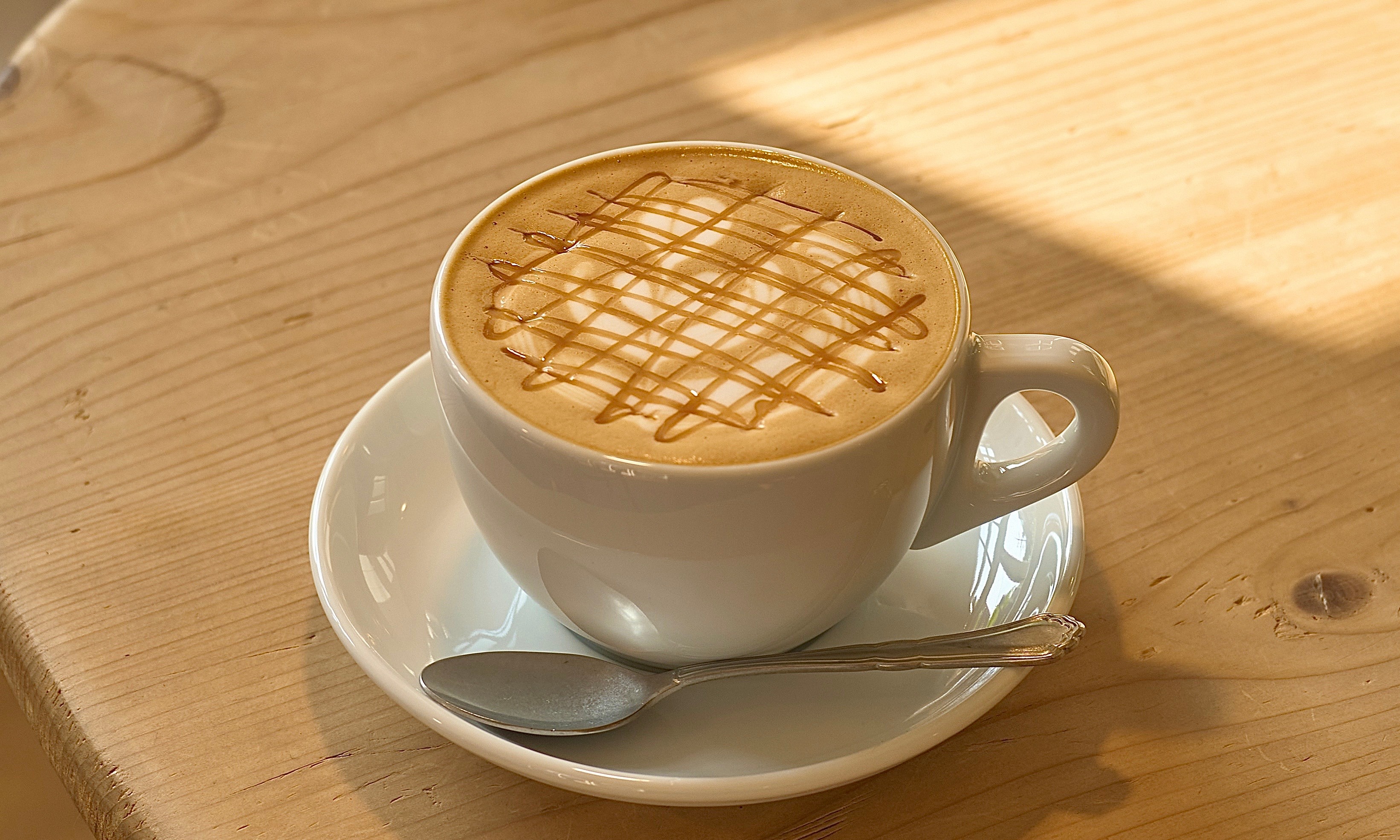 Ceramic cup of warm latte with caramel drizzle on a natural grain wooden table