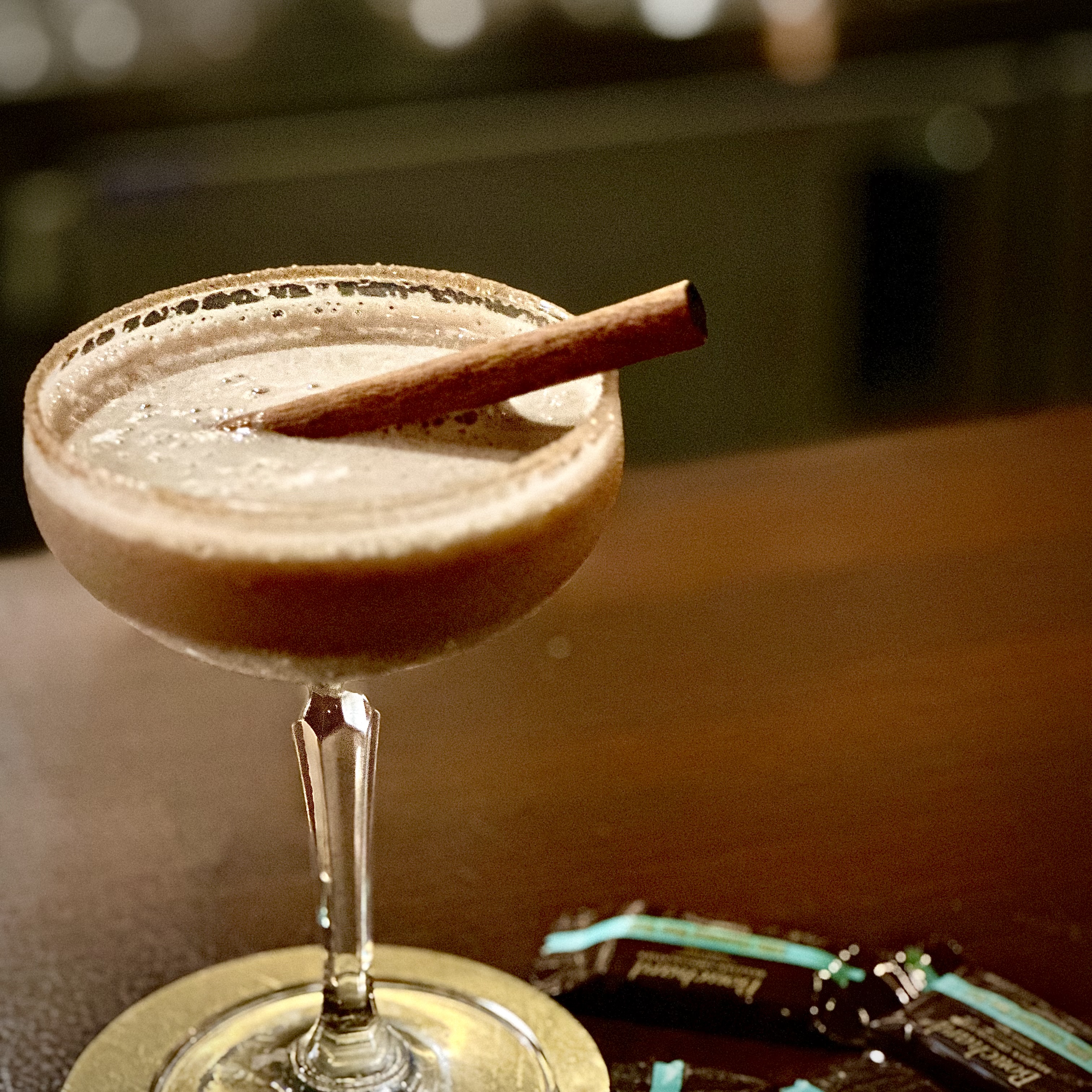 A specialty cocktail served in a coupe glass with a cinnamon stick garnish