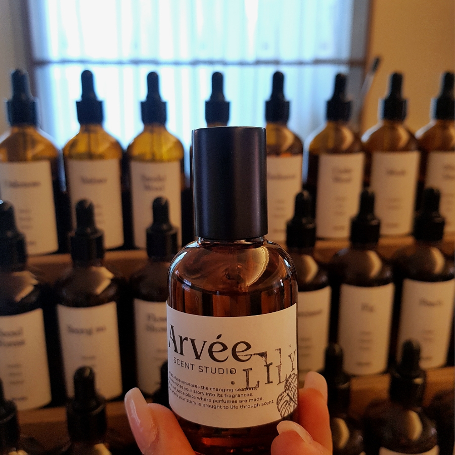 Hand holding a custom perfume flacon labeled Arvee Scent Studio in front of workshop shelves