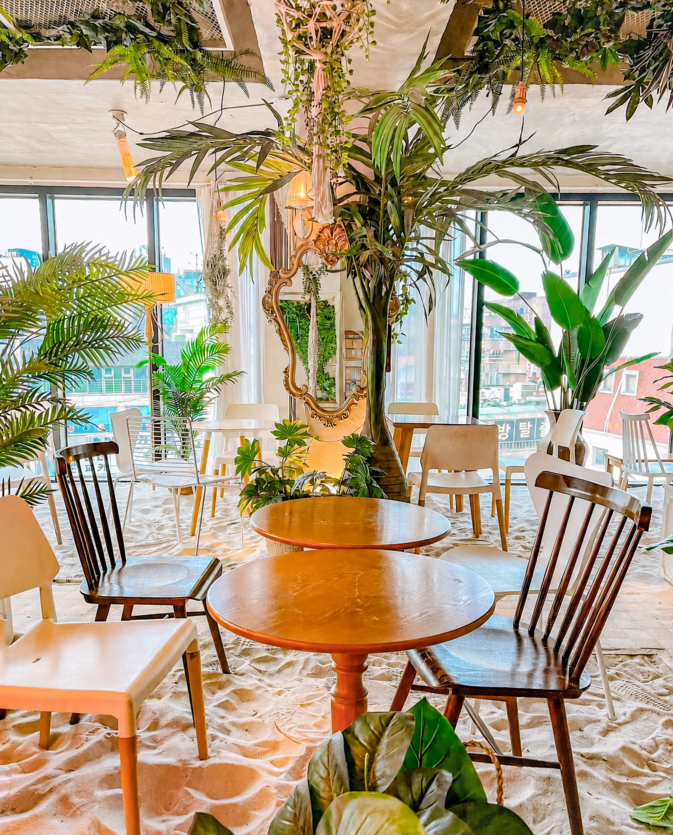 Indoor beach lounge with soft sand floor, tropical plants, and warm hanging pendant lighting