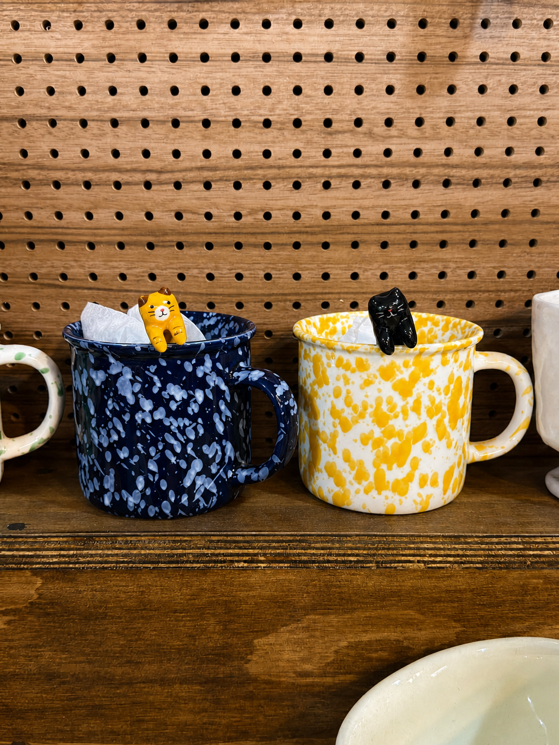 Handmade navy and yellow ceramic mugs displayed against a wooden pegboard wall at Yeoul.