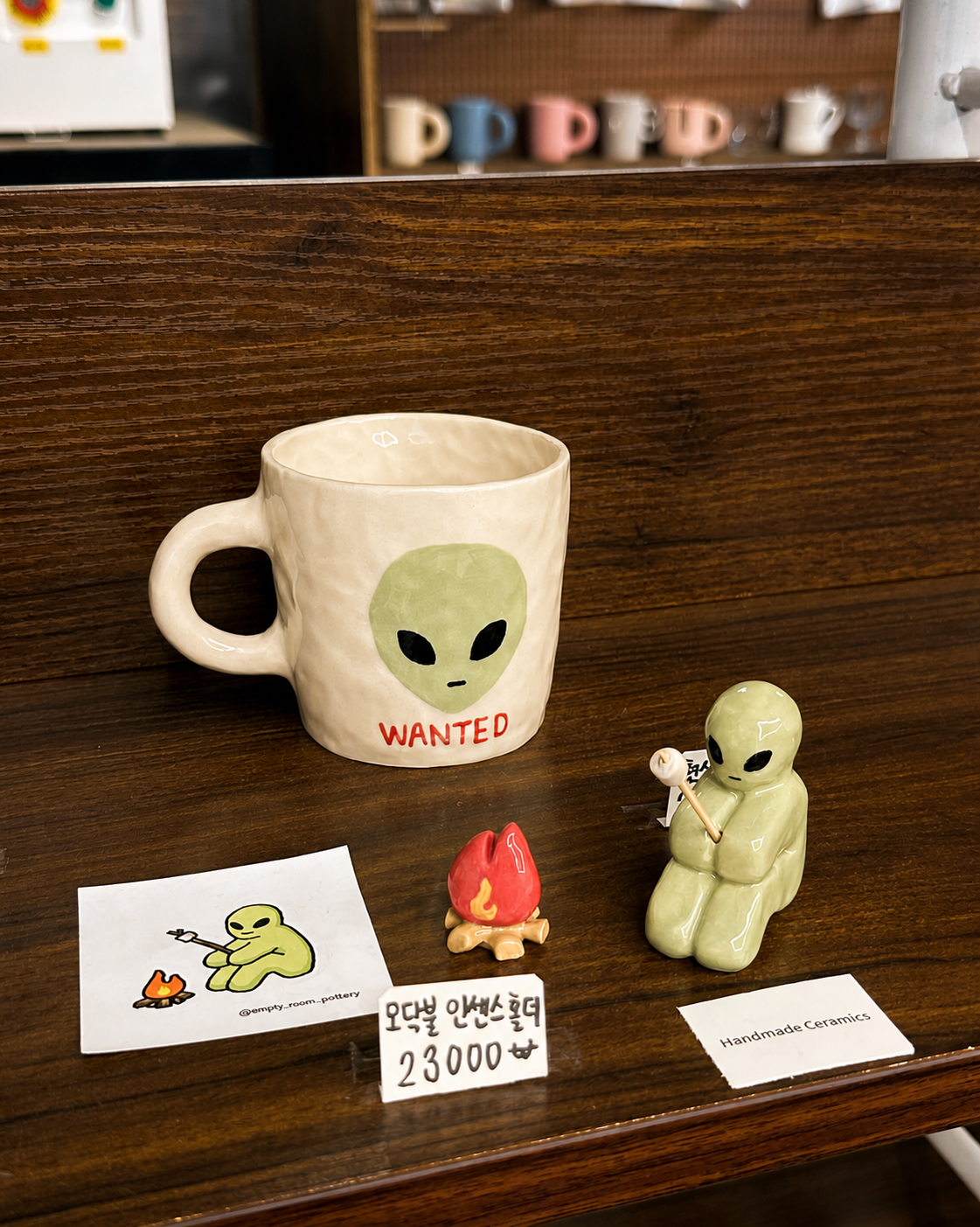 Handmade alien ceramic mug and small ceramic figures displayed on a wooden shelf at Yeoul.