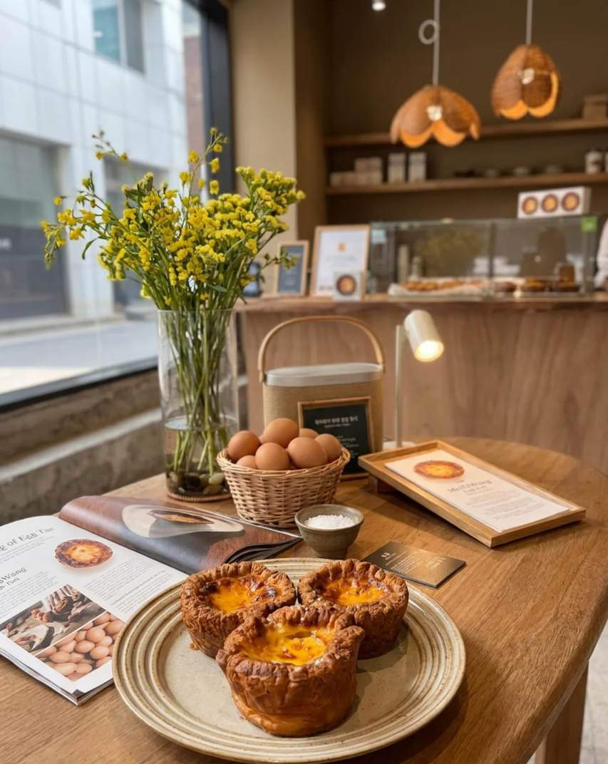 Three egg tarts on a plate with yellow flowers at the Myeongdong store, set on a wooden table